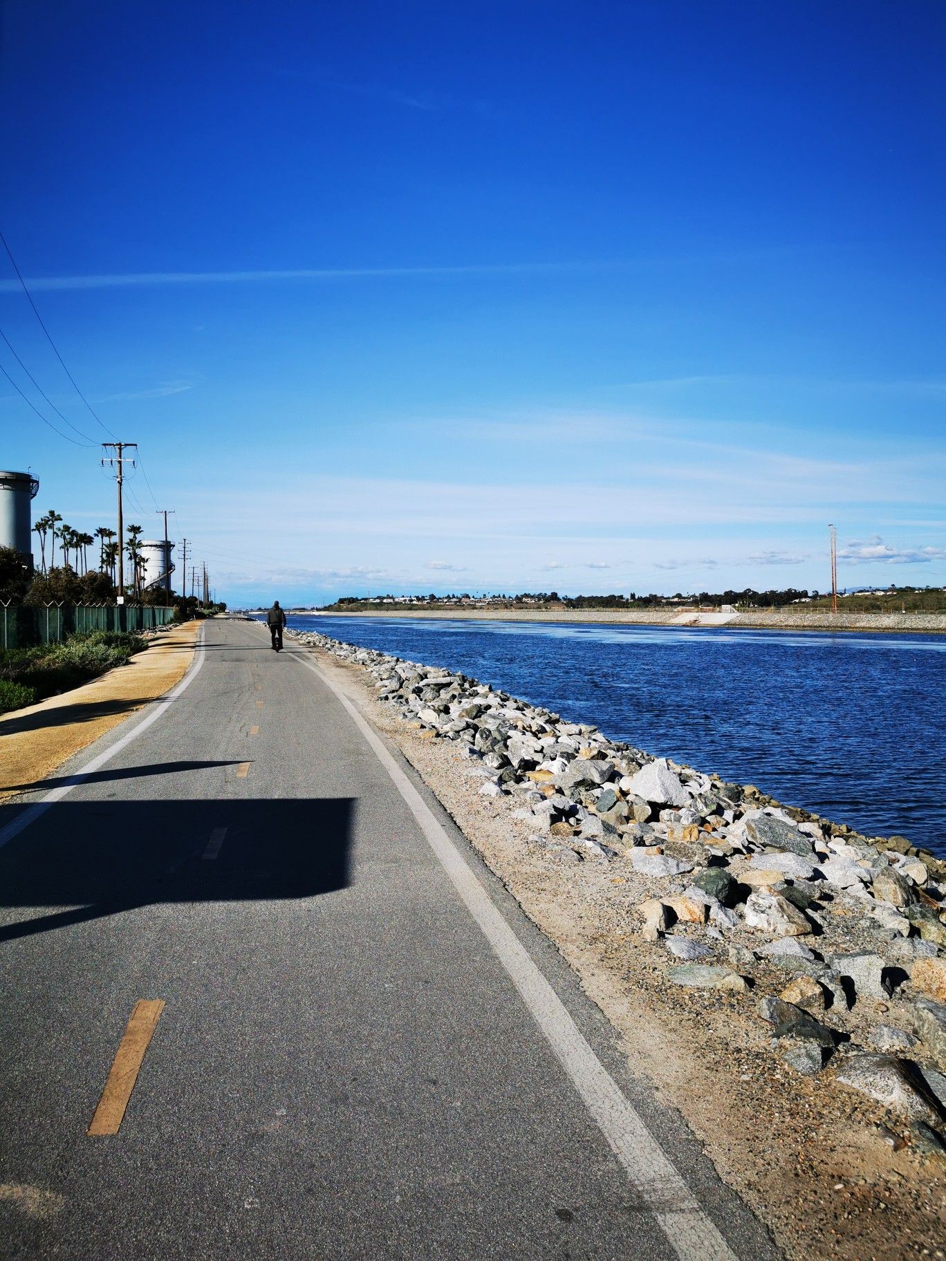A person walks on a paved path beside a river under a bright sky. - Santa Ana River Trail and Fairview Park Loop