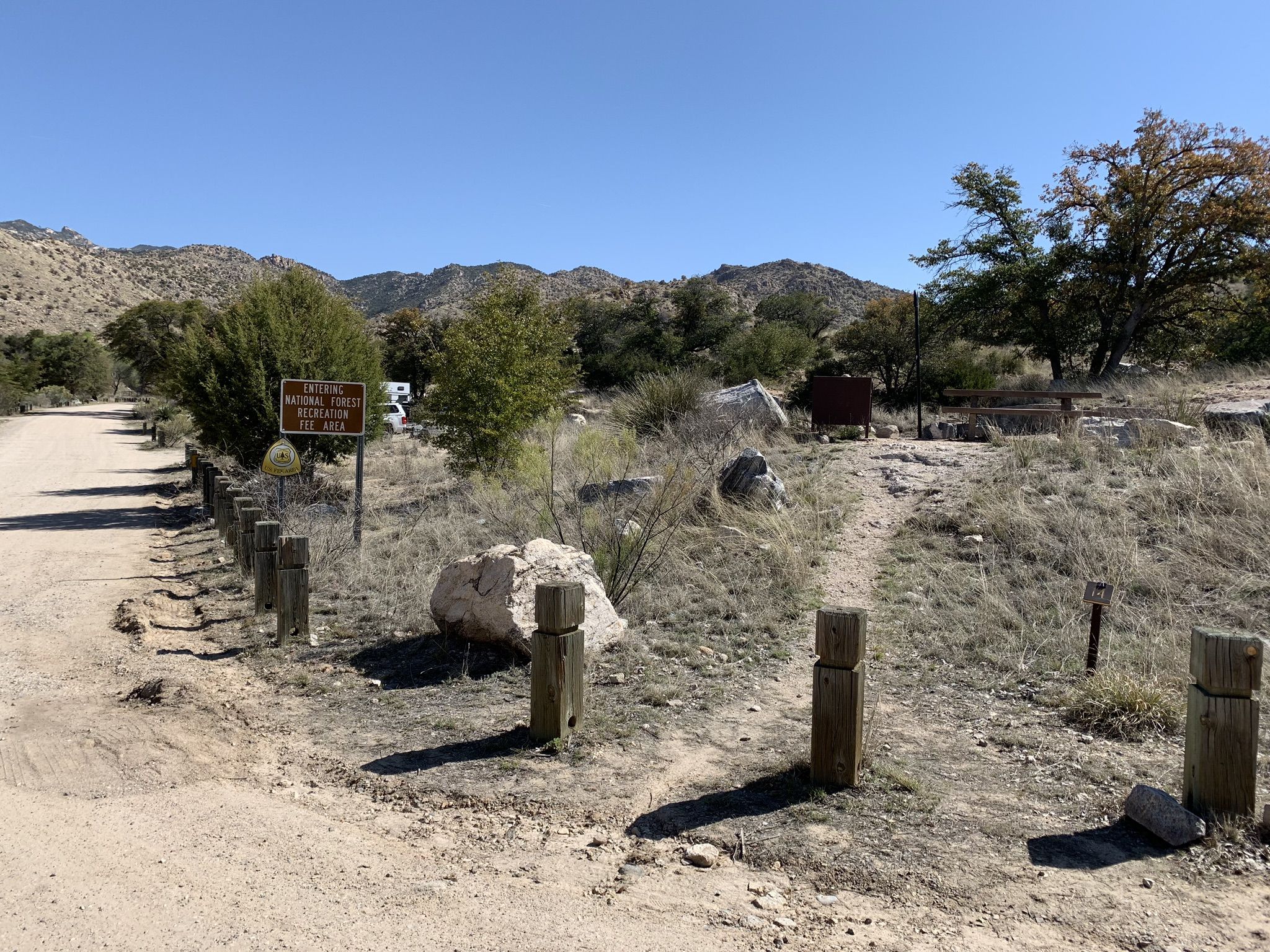 A dirt road with wooden posts and a sign under a clear, sunny sky. - Gordon Hirabayashi Campground loop from Molino Basin Campground