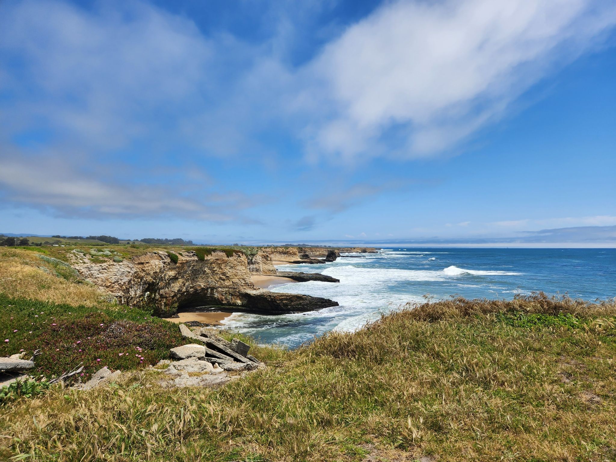 Sunny view of green grassy cliffs overlooking a blue ocean with crashing waves. - Sand Point Beach Overlook – Needle Rock loop from Wilder Dairy Cultural Preserve