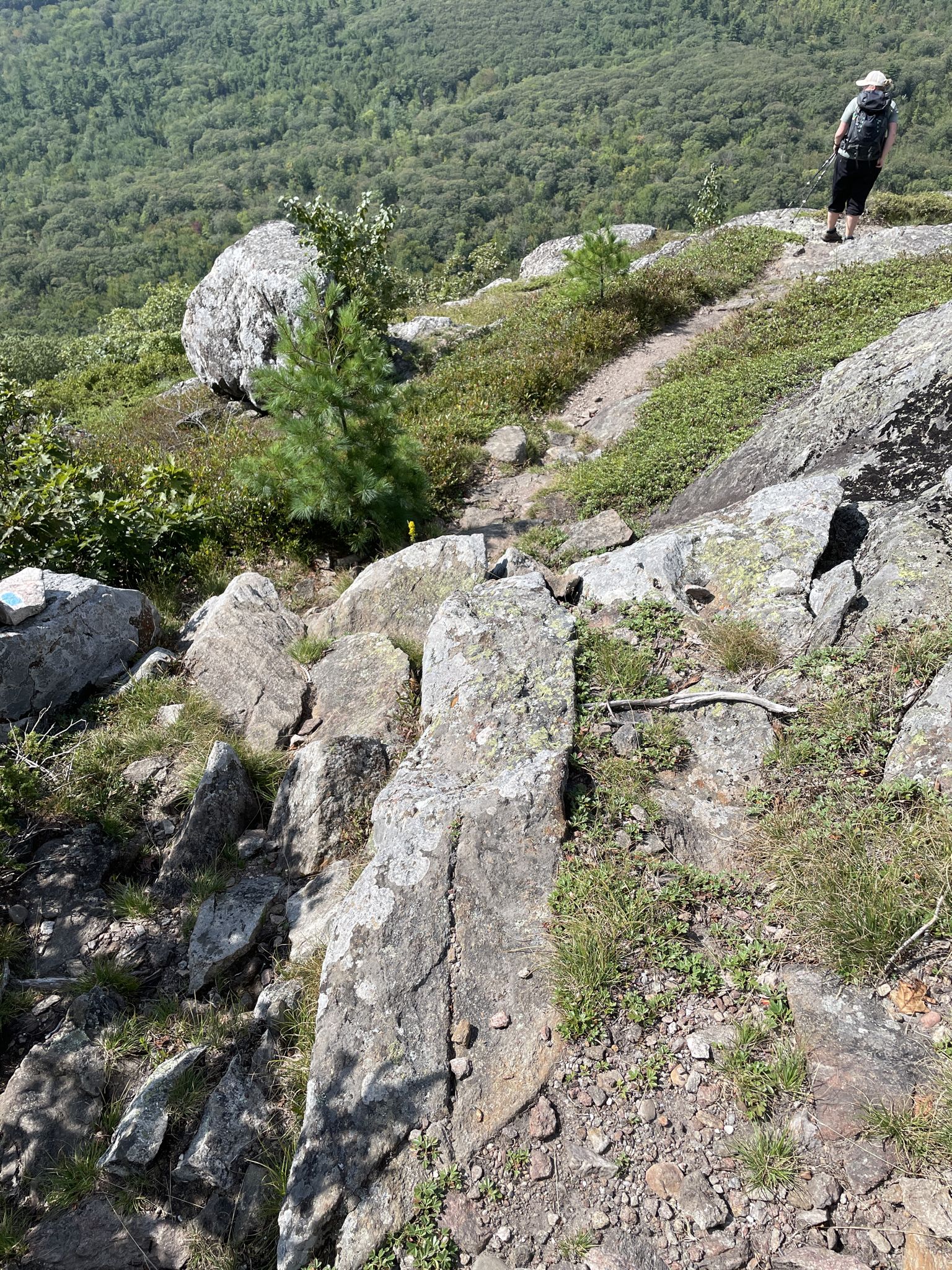 Hiker stands on a rocky mountain trail overlooking a forested valley. - Little Ragged and Ragged Mountain Loop