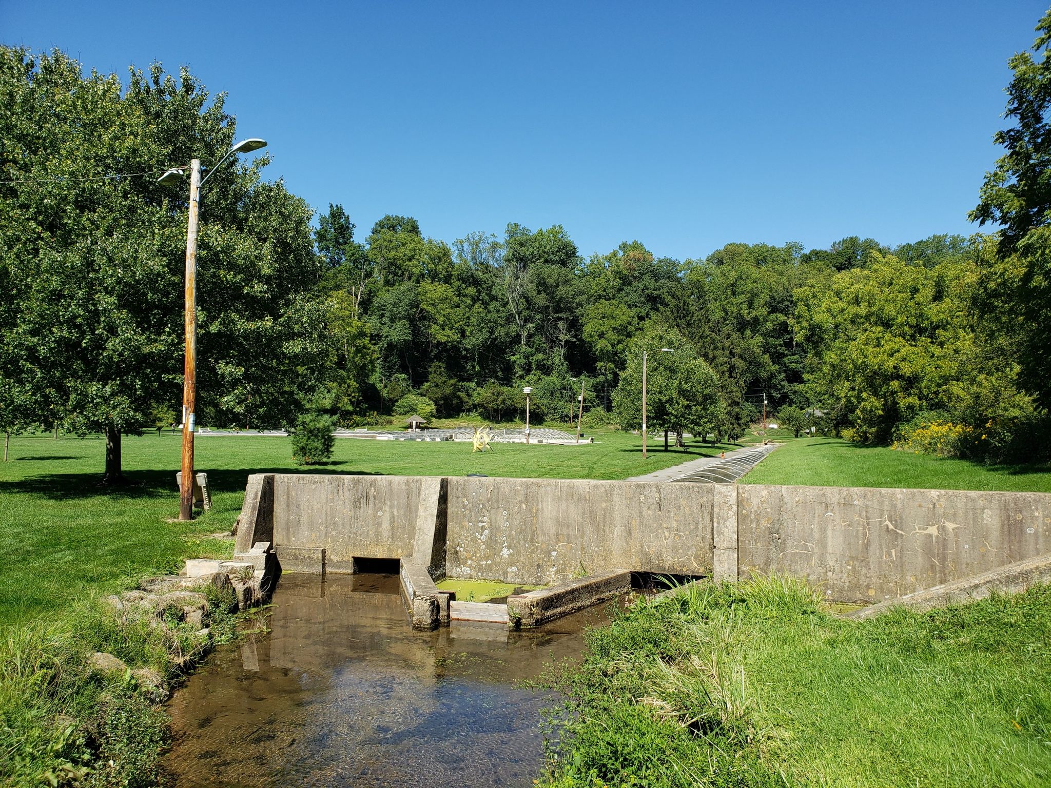 Sunny view of a concrete dam and stream in a green park with trees. - Bogert Covered Bridge loop from Lehigh Valley Hospital