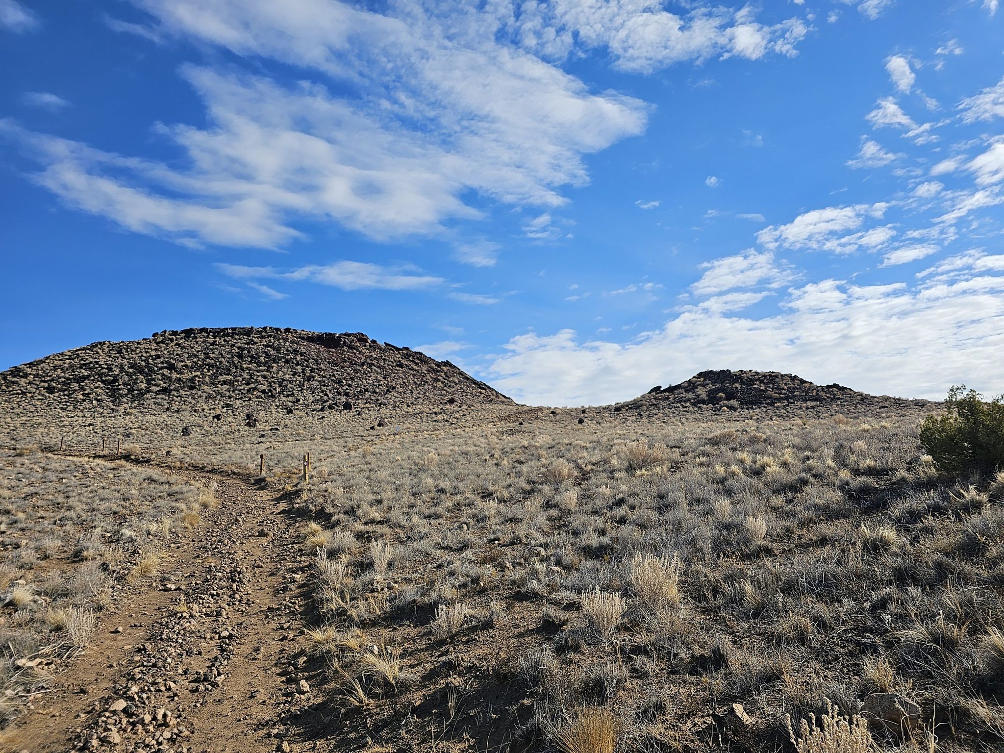 Dirt path leading towards two rocky hills under a partly cloudy sky. - Volcanoes Trail loop