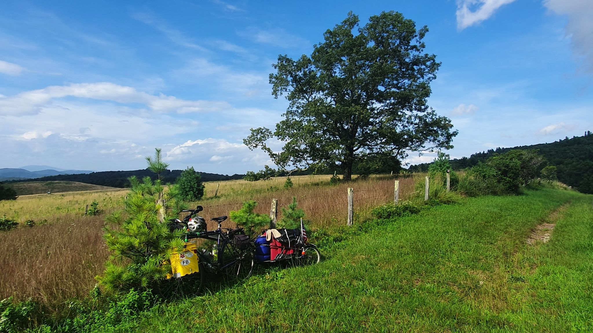 Two touring bicycles parked in a sunny grassy field with distant hills. - Brinegar Cabin to Air Bellows Overlook — Blue Ridge Parkway