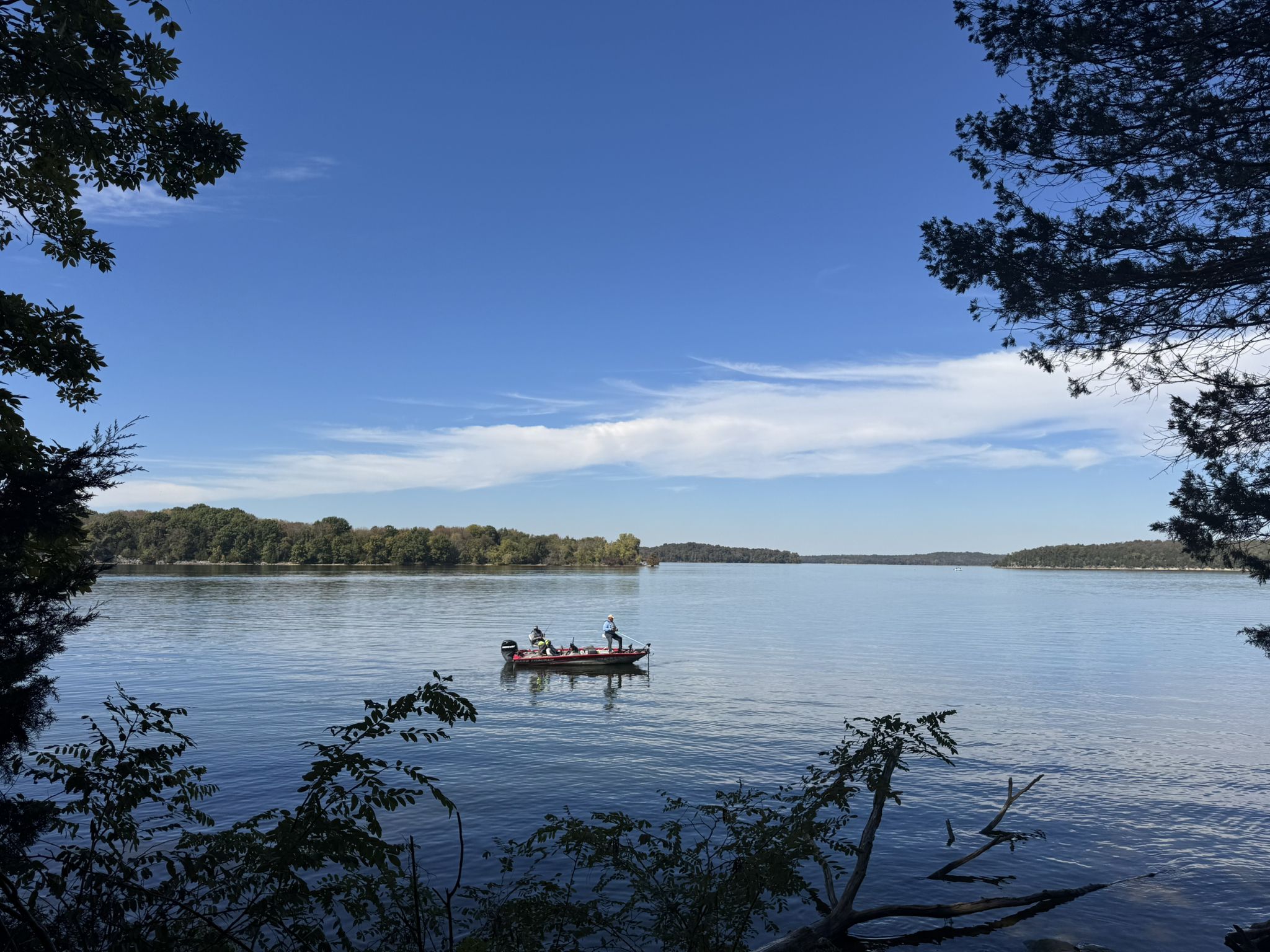 People fishing from a boat on a wide lake under a clear blue sky. - Day Loop Trail