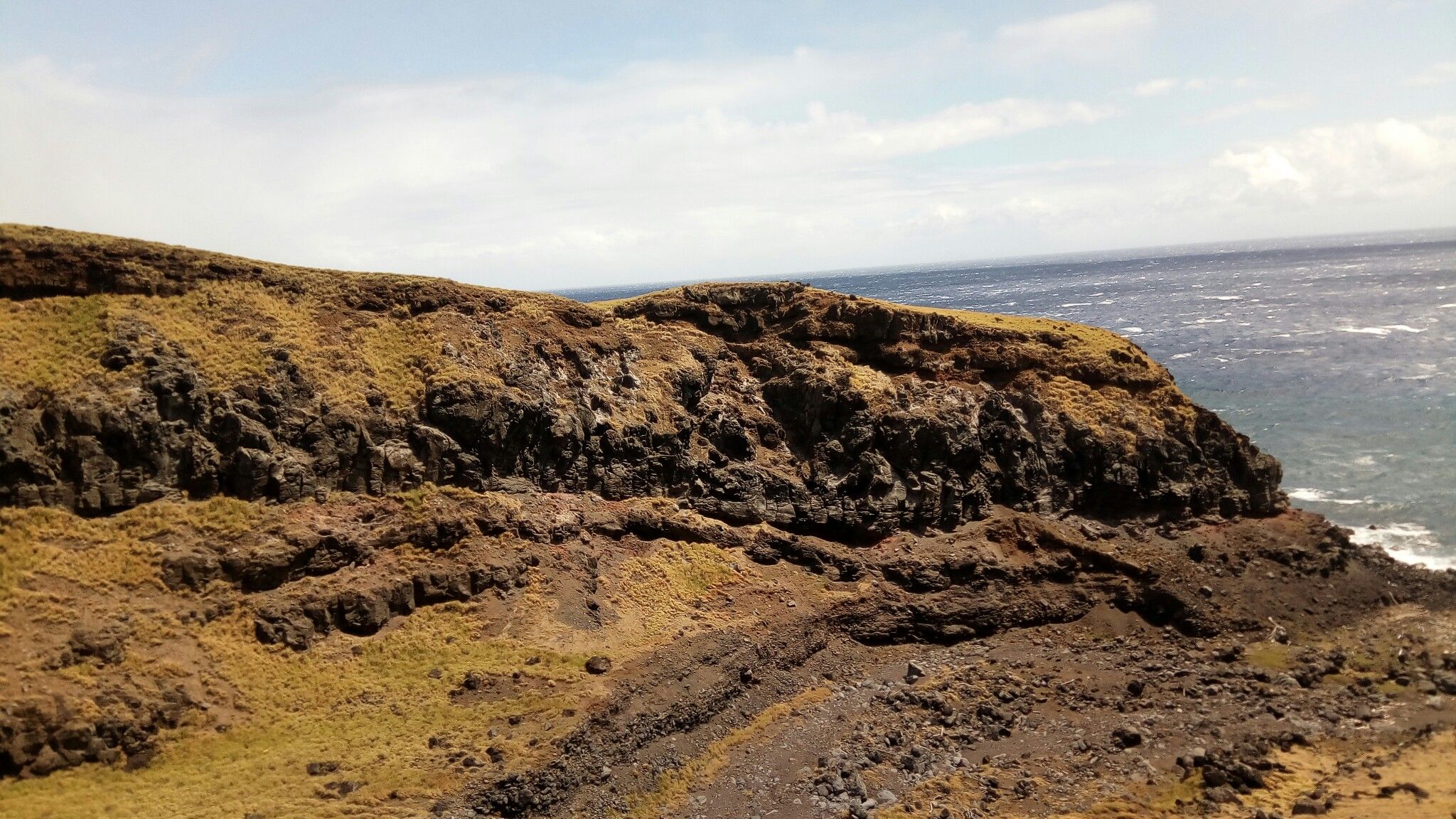 Rocky, grassy cliff overlooking a choppy ocean under a partly cloudy sky. - Piilani Highway via Ulupalakua