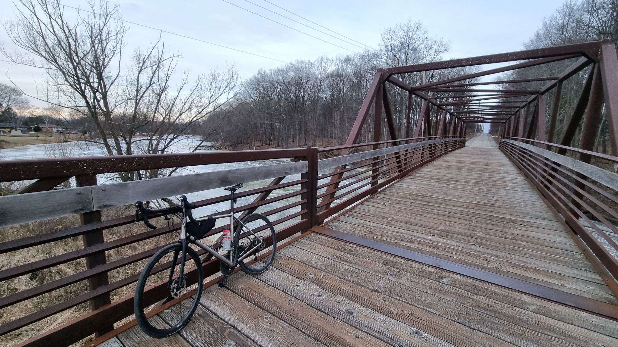 A bicycle rests on a long wooden and metal bridge over a river. - Fiddleheads Coffee – Port Washington loop from Scout Park