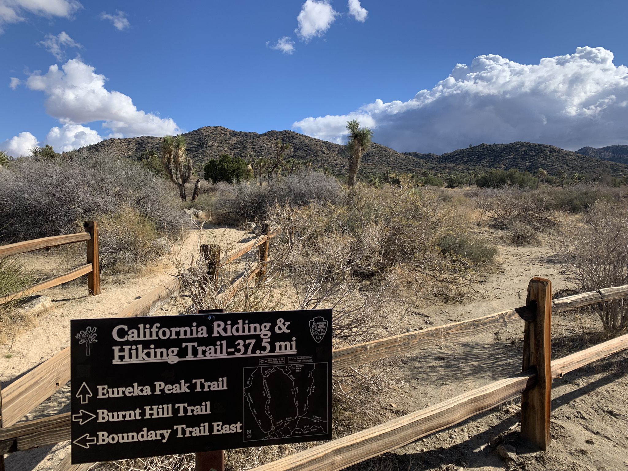 A trail sign and wooden fence in a desert landscape with hills and clouds. - Running loop from Black Rock Backcountry Registration Board