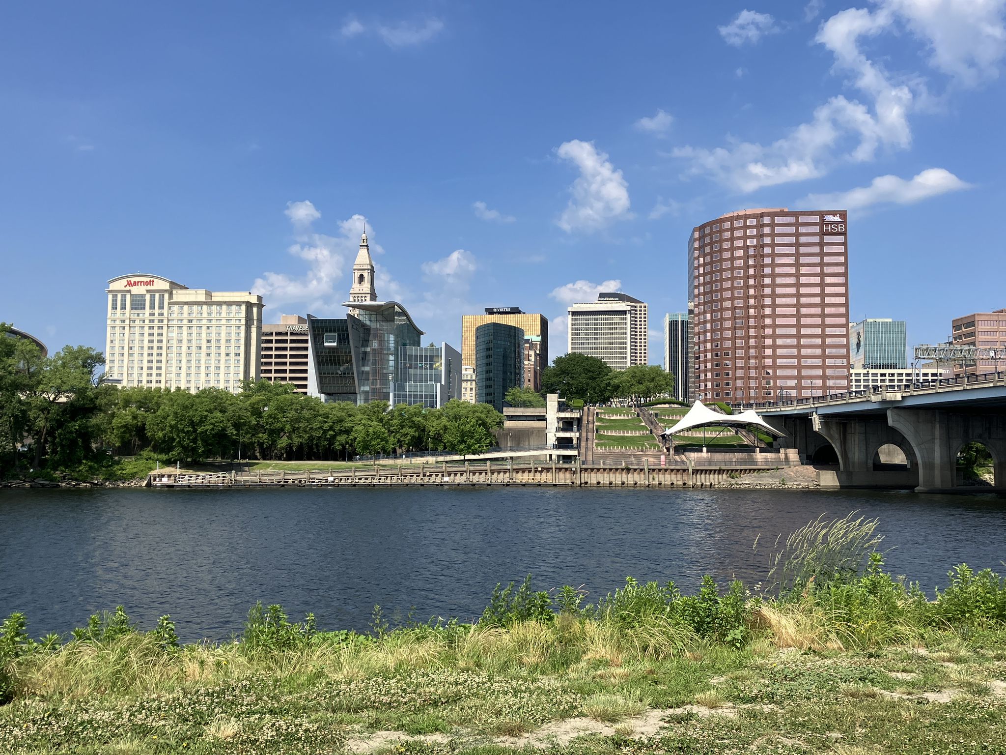 A city skyline and bridge overlook a wide river on a sunny day. - Charter Oak Greenway