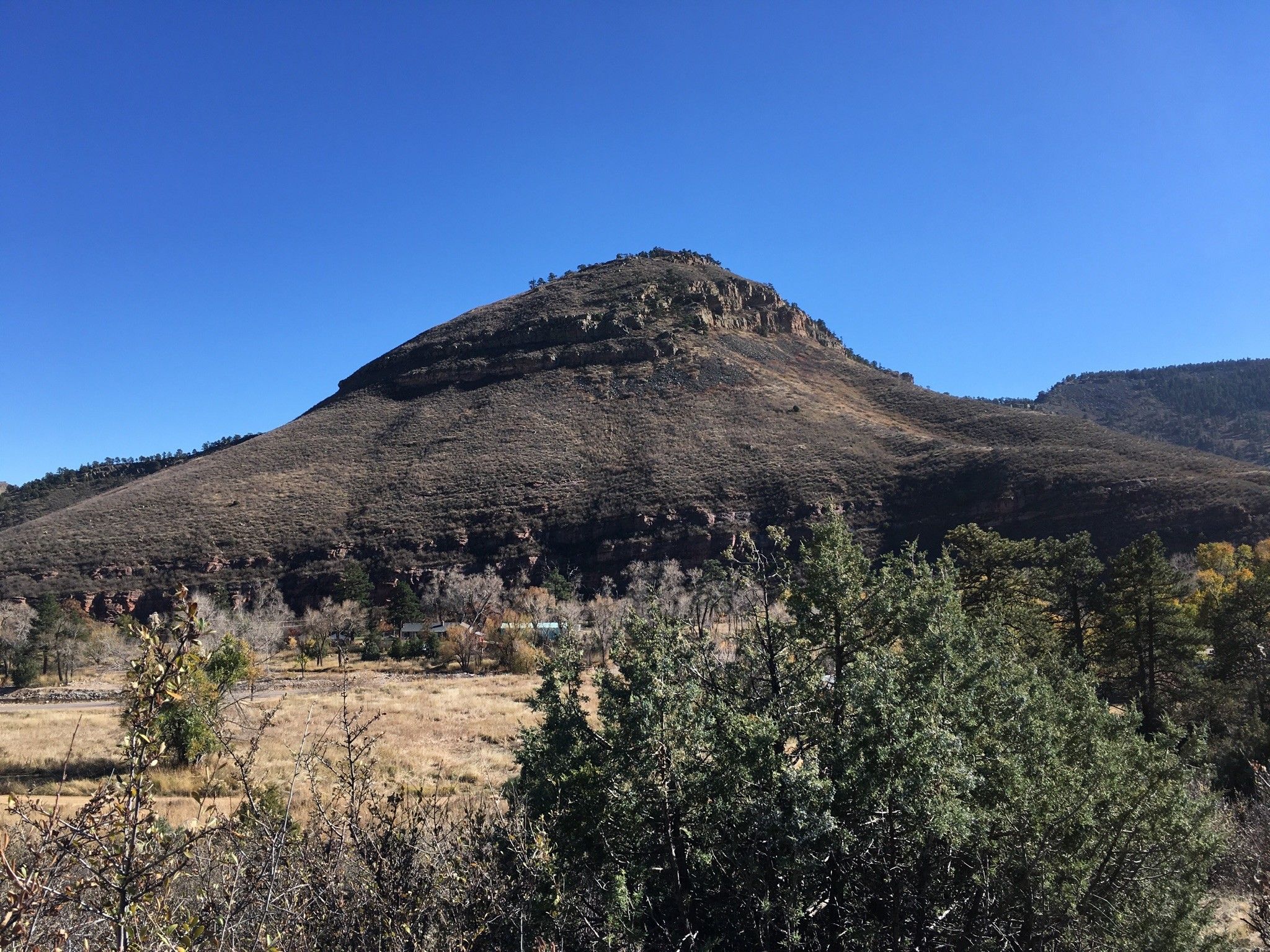 Large, dark mountain dominates a dry, treed landscape under a clear blue sky. - Hall Ranch Loop: Nighthawk and Bitterbrush Trail