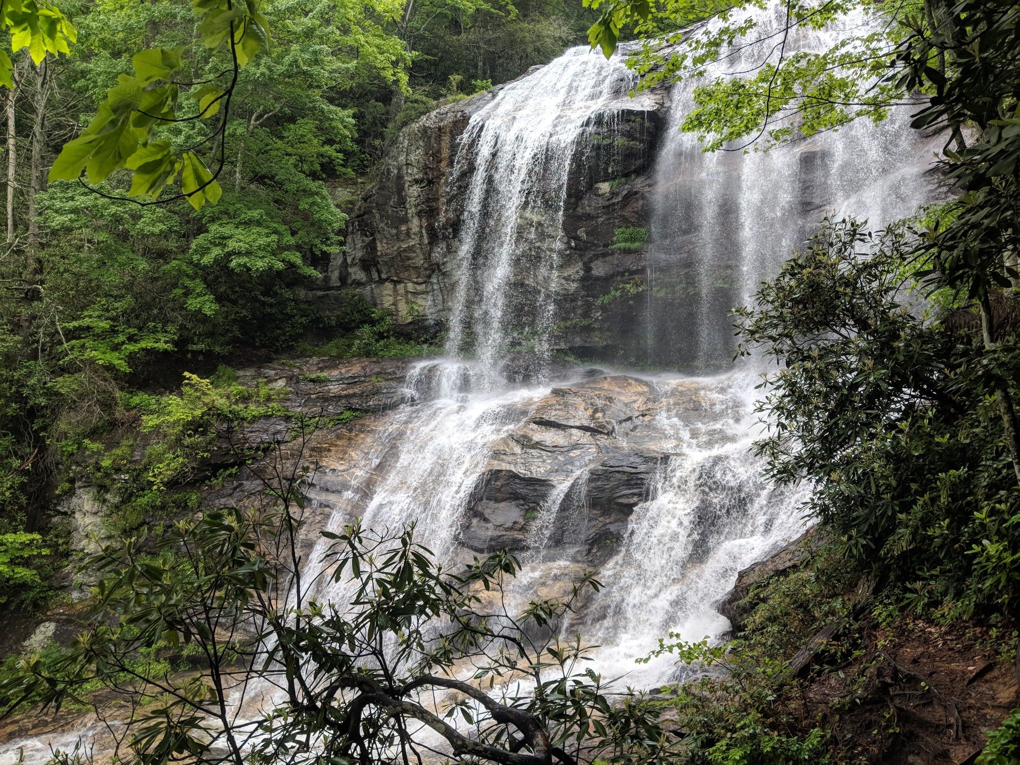 Tall, multi-tiered waterfall cascades down dark rocks in a green forest. - Glen Falls loop from Glen Falls