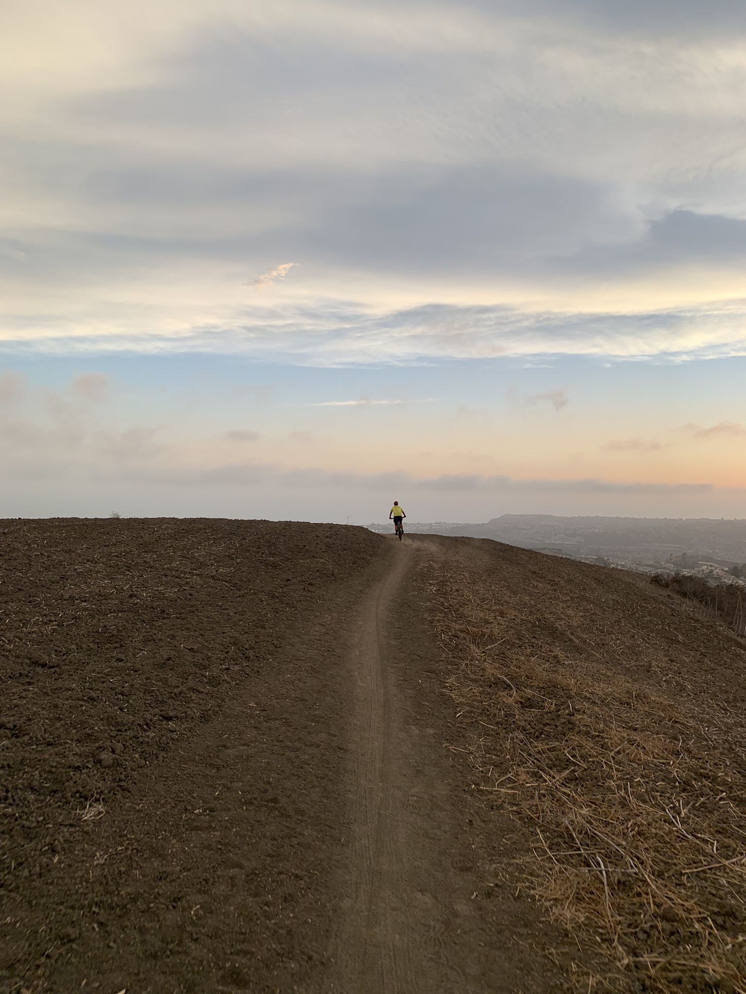 A person runs on a narrow dirt path along a ridge at dusk. - North Los Mares, Prima Desecha, and Las Ramblas Trail