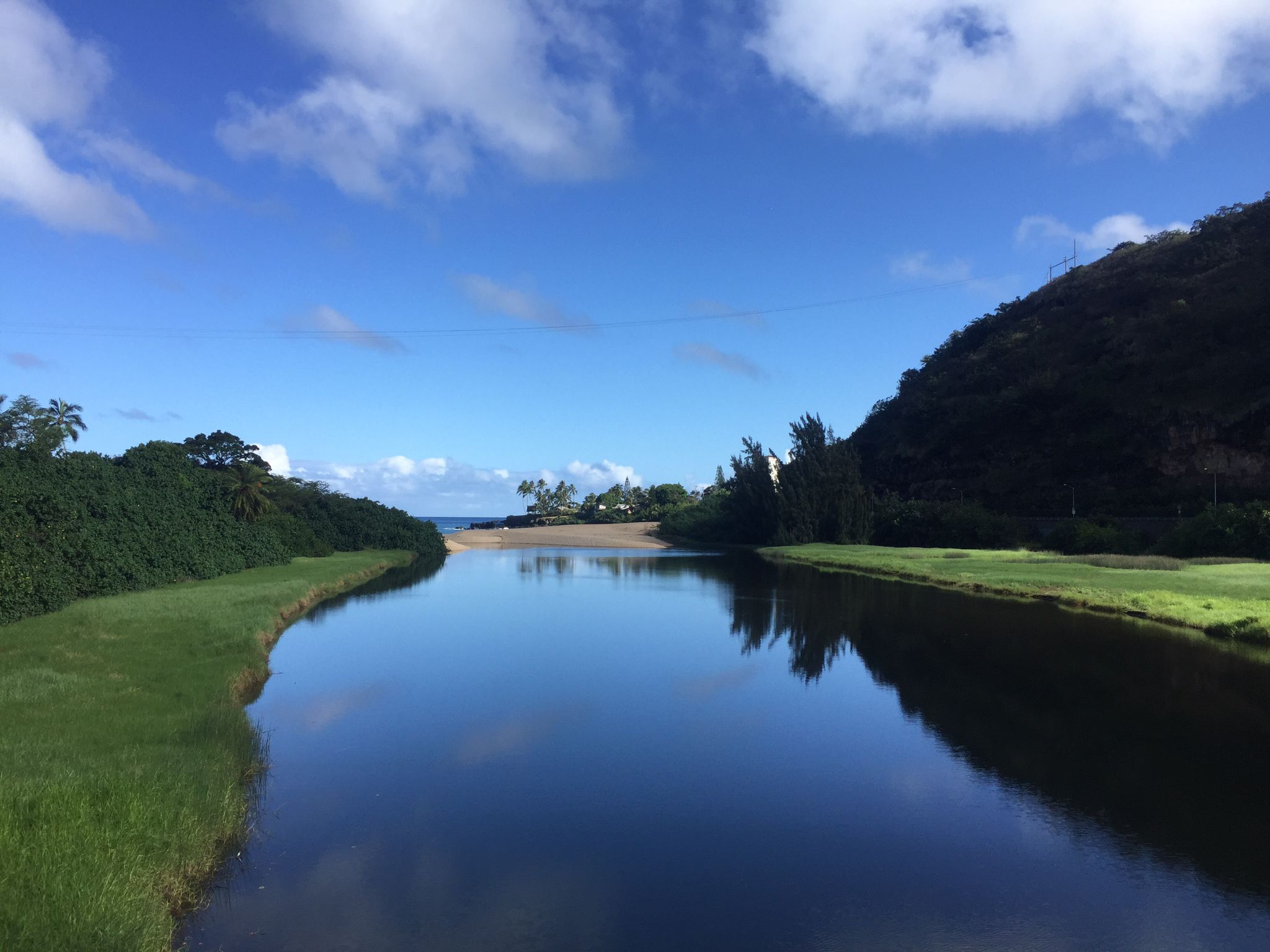 Calm river reflecting blue sky, flowing between green banks towards the ocean. - Ke Ala Pūpūkea Bike Path