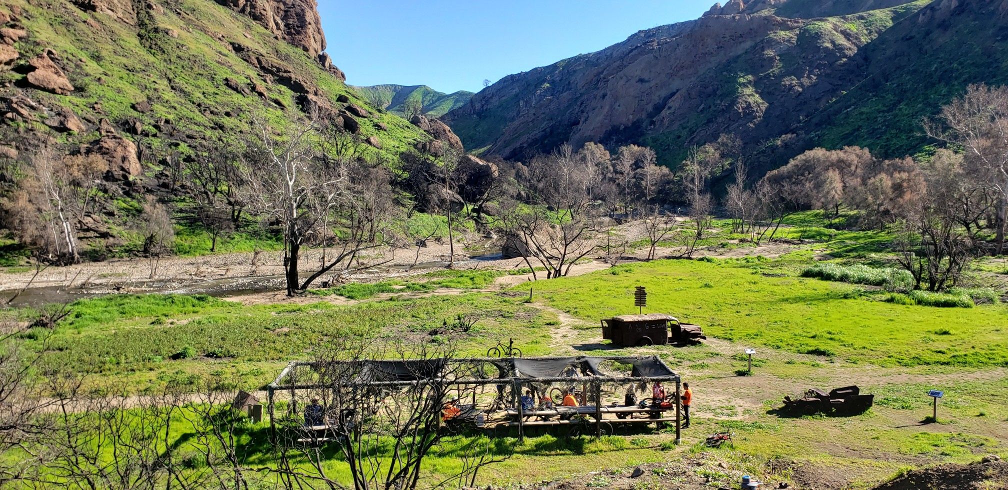 Green valley with mountains, bare trees, and a structure in bright daylight. - Malibu Creek State Park loop