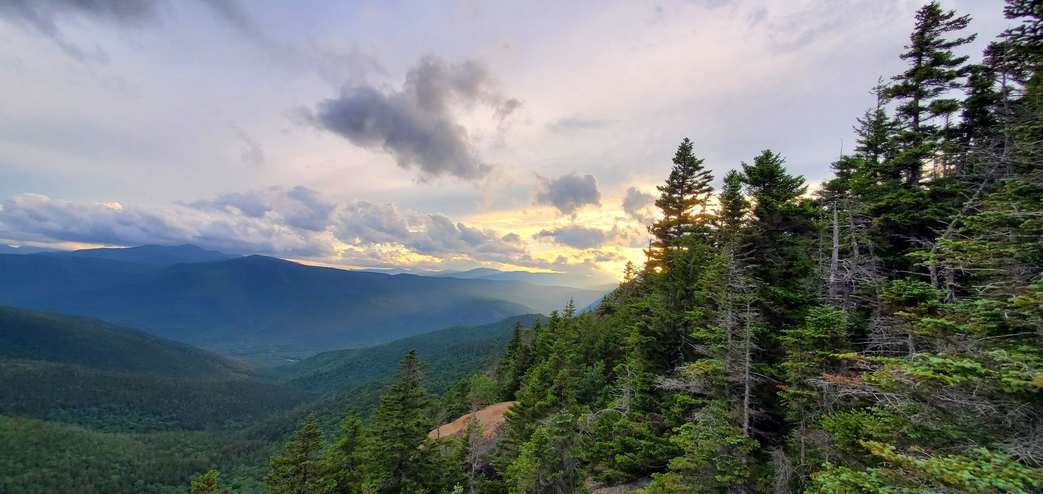 Sunlight breaks through clouds over a vast mountain range and evergreen forest. - Mount Crawford, Stairs Mountain, and Mount Resolution