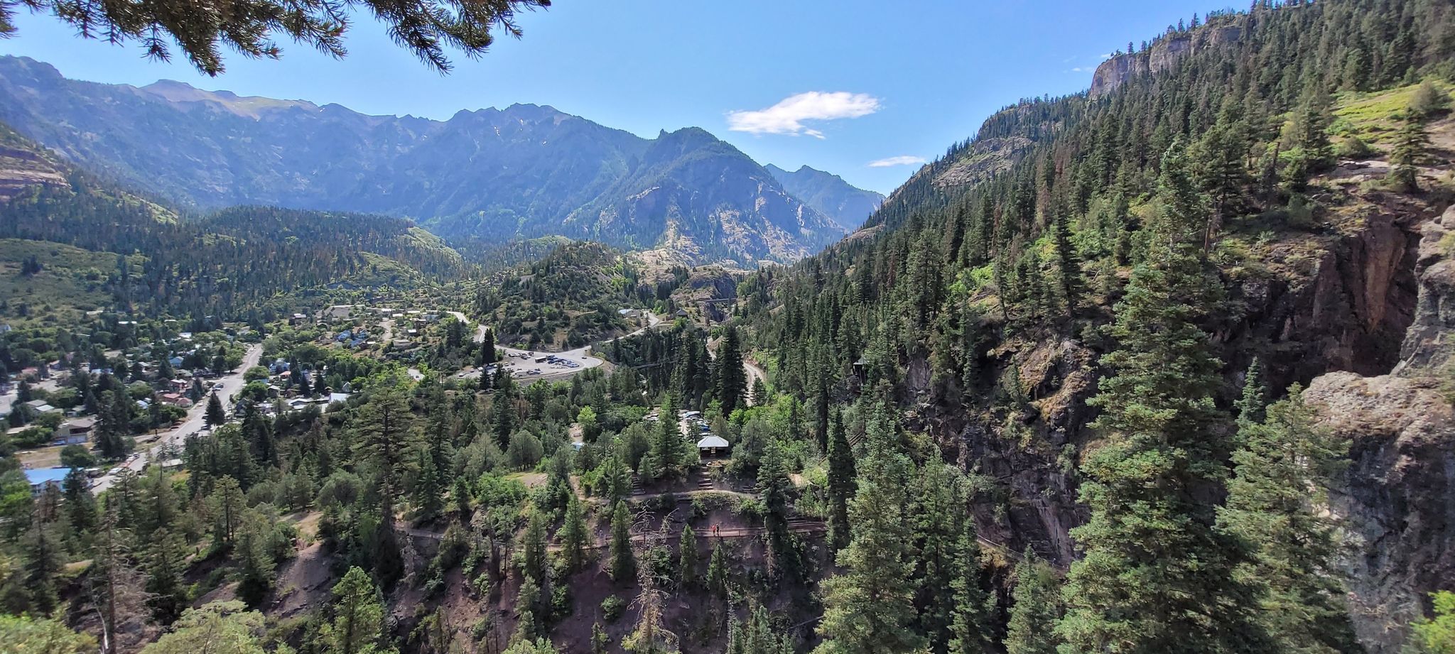 A panoramic view of a mountain valley with dense green forests and distant buildings. - Ouray Perimeter Trail