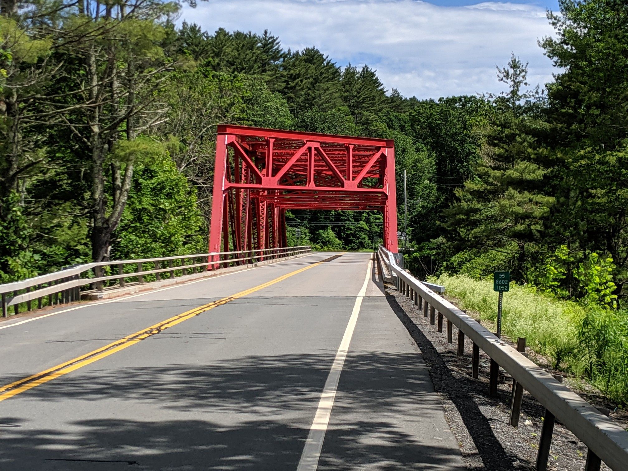 Bright red truss bridge spanning a paved road through a green forest. - Rondout Reservoir – Neversink Reservoir loop from 