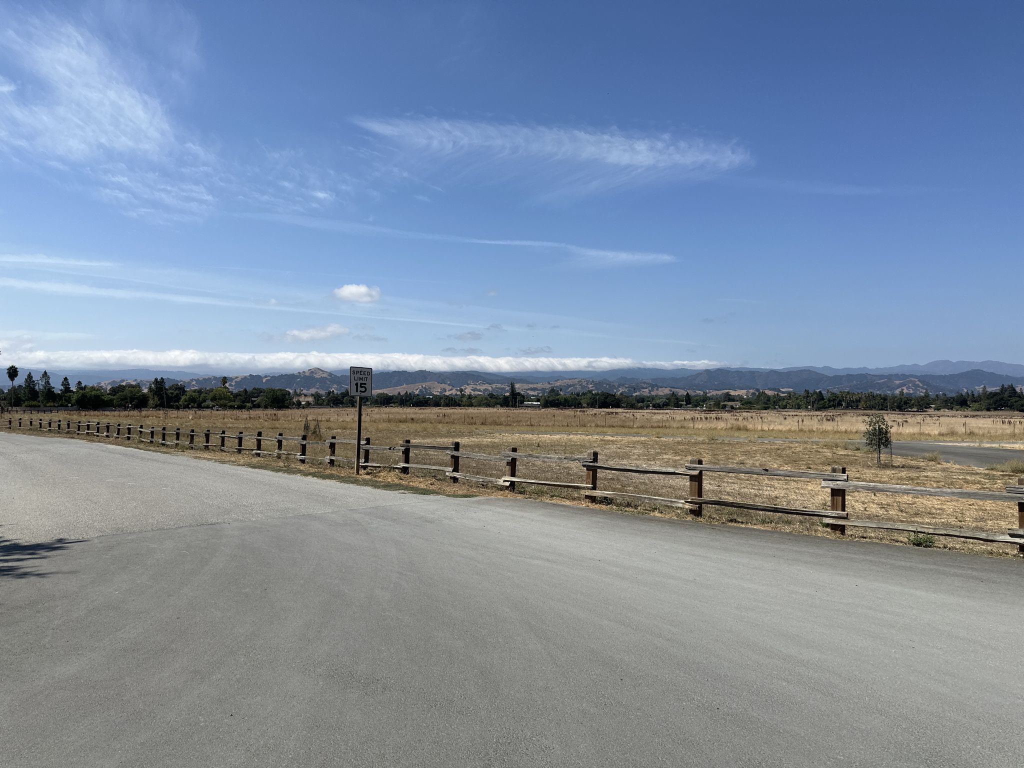 Paved road next to a wooden fence, dry fields, and distant mountains. - Coe Ranch Headquarters – China Hole Trail loop from Morgan Hill