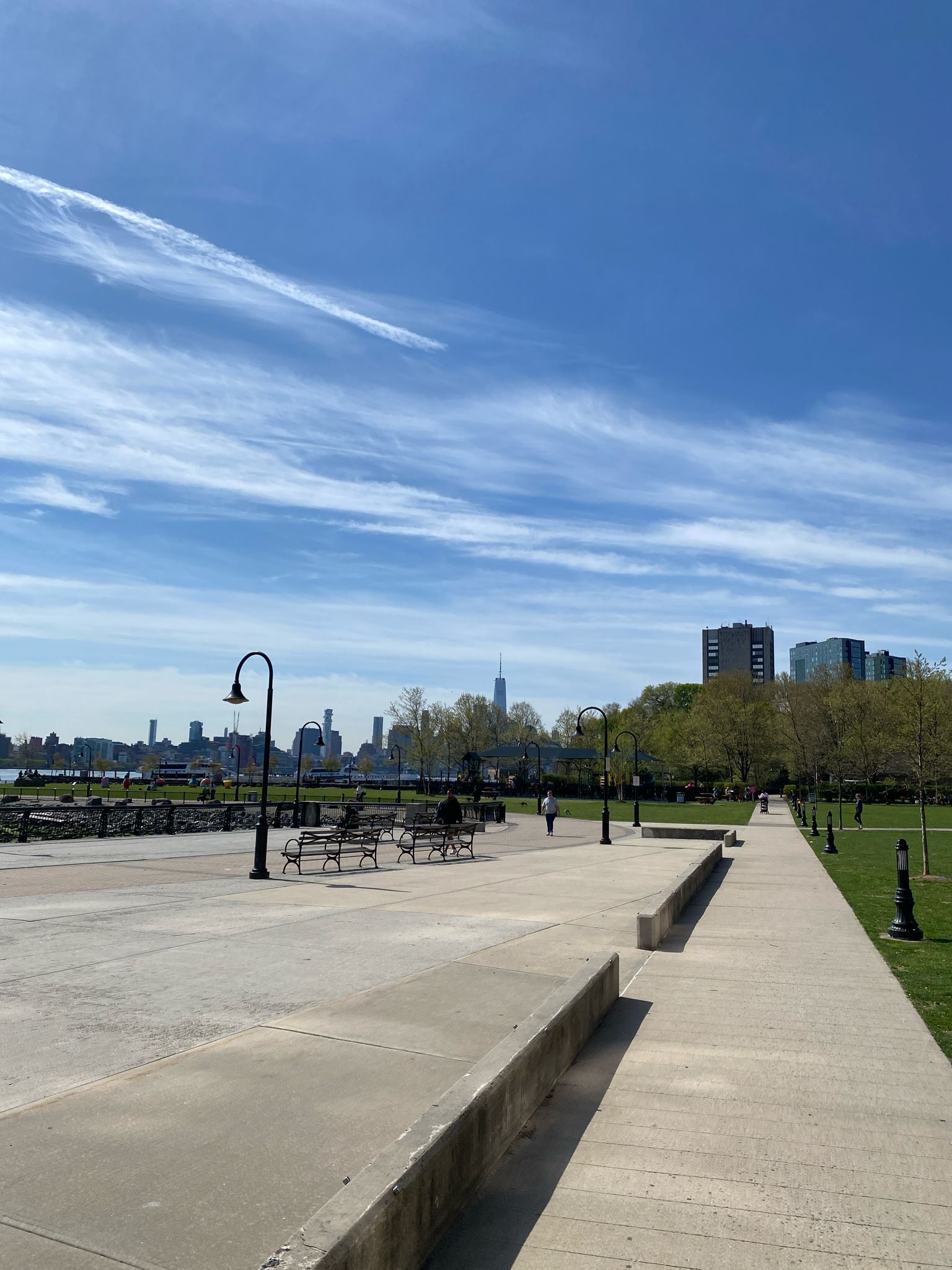 Paved waterfront path with benches, distant city skyline under a clear sky. - Weehawken Cove loop from Lincoln Harbor