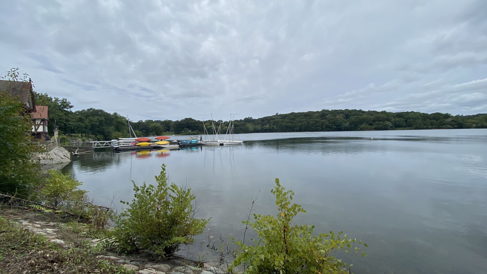 A lake with boats docked at a boathouse under an overcast sky. - Walking City Trail: Section 3