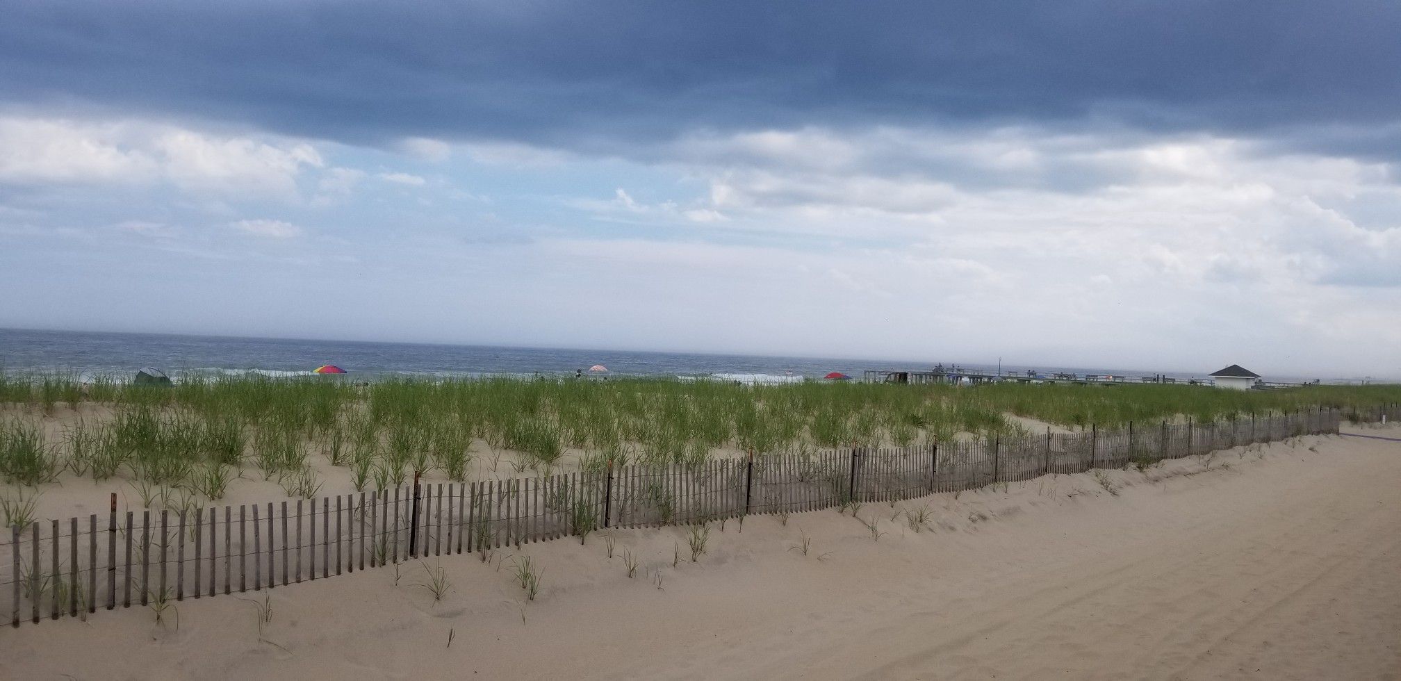 Ocean view with sandy dunes, green grass, and a cloudy sky. - Bradley Beach Boardwalk & Wesley Lake loop