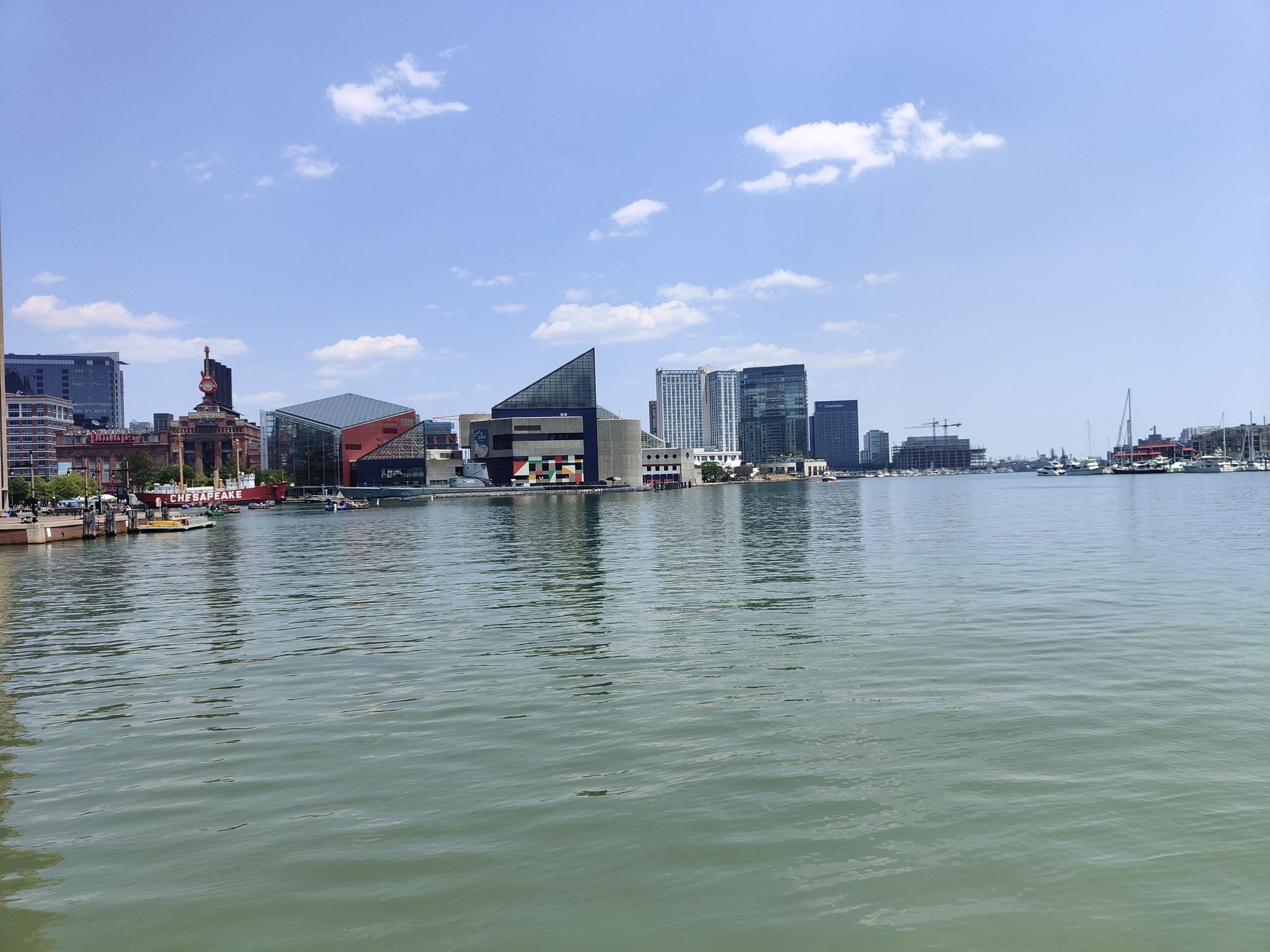 Wide view of a city skyline across calm water under a clear blue sky. - Jones Falls – Baltimore Waterfront loop from Highlandtown