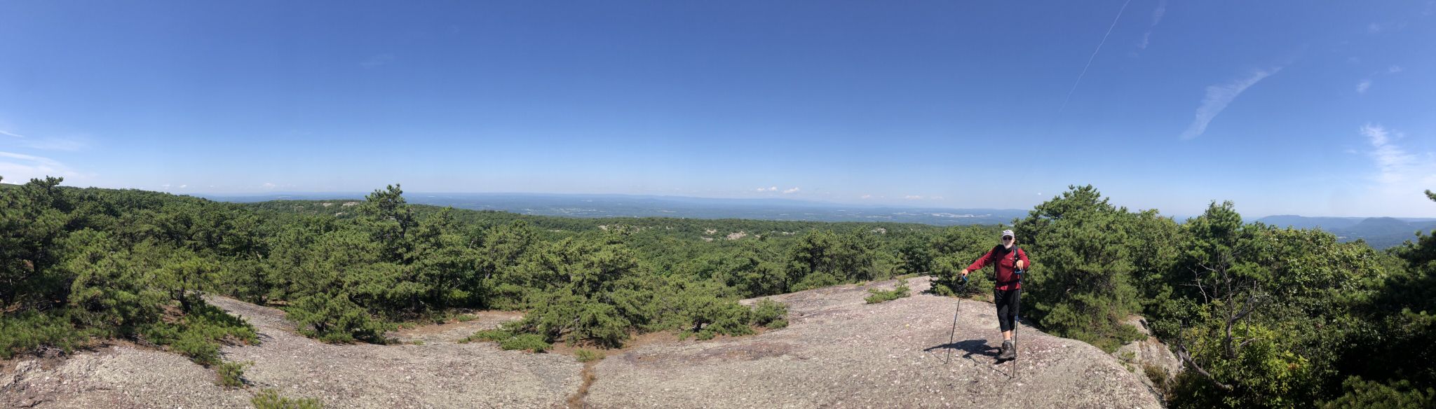 A hiker with poles stands on a rocky overlook with a vast sunny forest panorama. - Hiking loop from Salisbury Mills