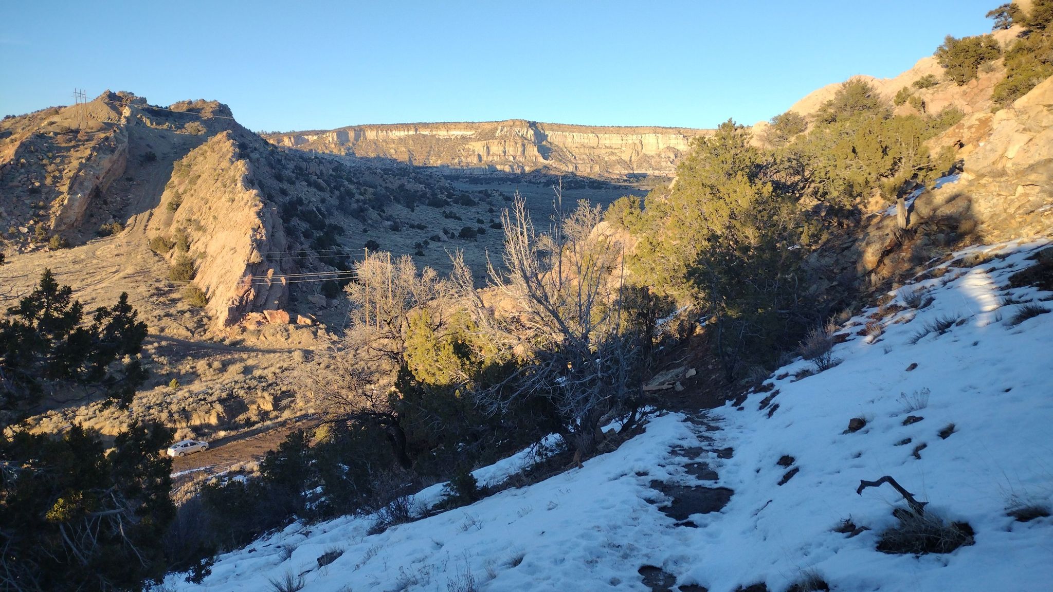 Sunny canyon landscape with snow-dusted hills and distant mesa under clear sky. - North Hogback Trail Loop