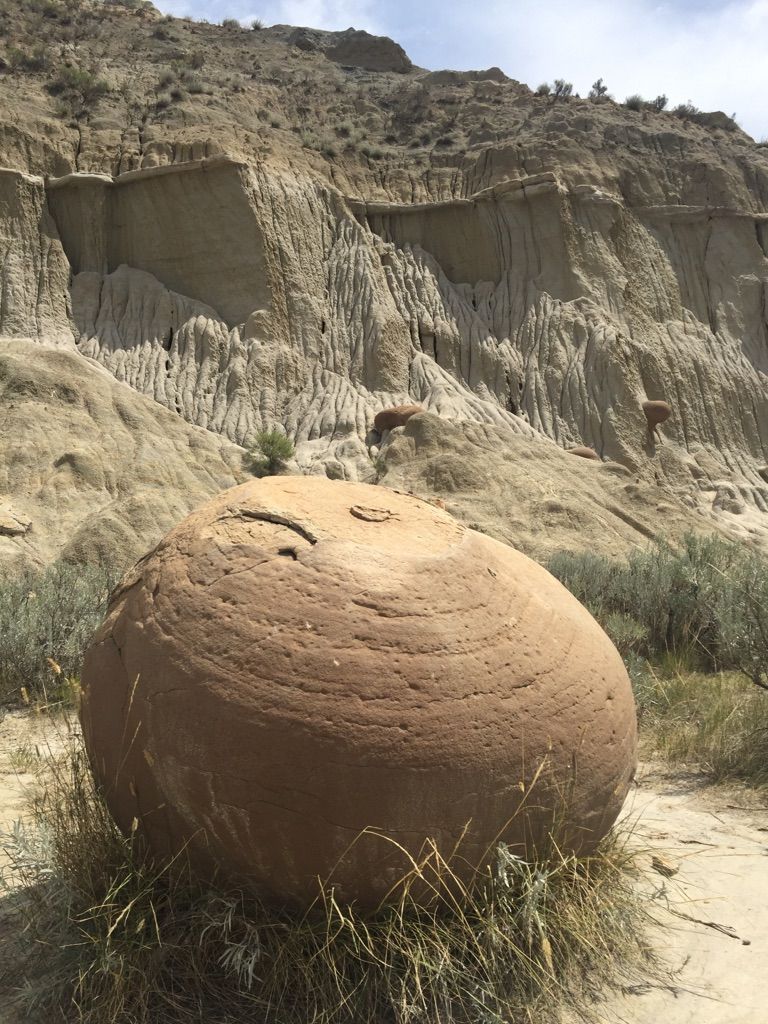 Large, spherical rock formation in the foreground with eroded badlands cliffs behind. - Buckhorn Trail