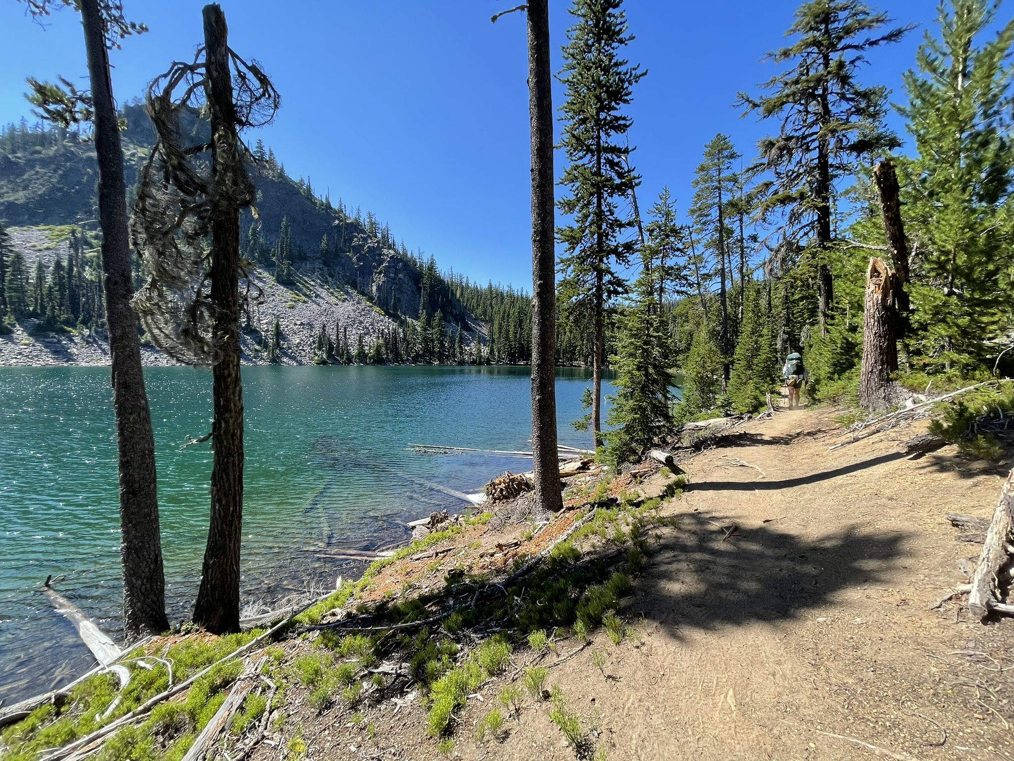 Clear blue lake with rocky mountains, dense forest, and a sunlit dirt trail. - Lower, Middle, and Upper Rosary Lake