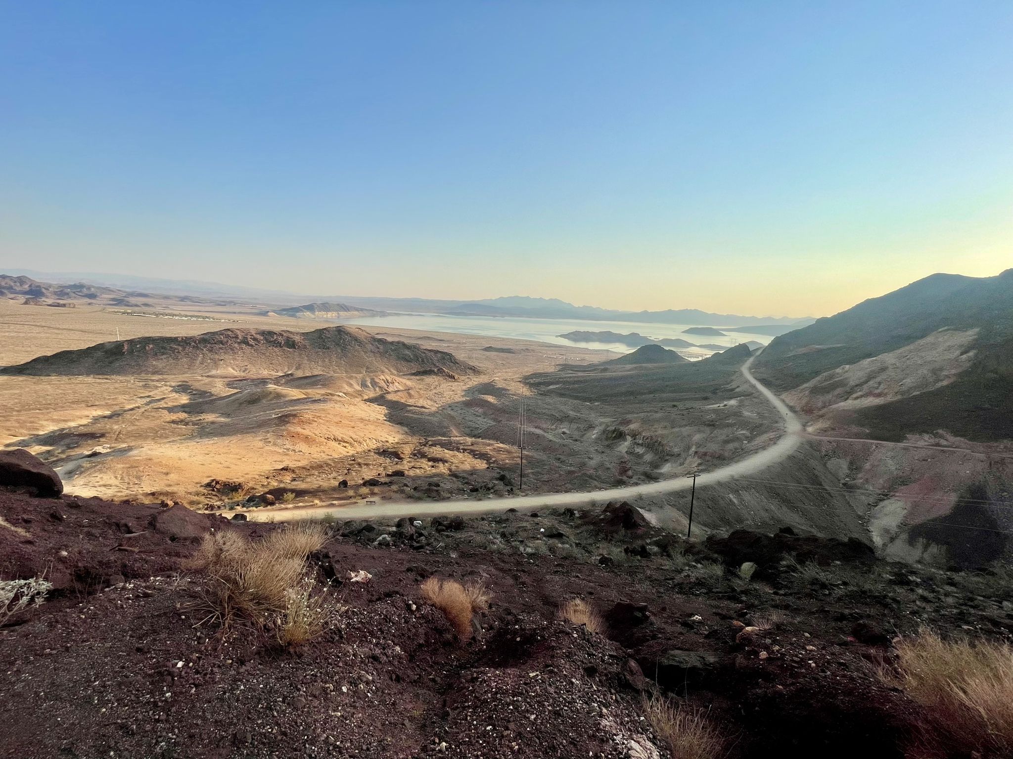 Winding road through arid hills overlooking a distant body of water. - Hoover Dam Lodge Trail