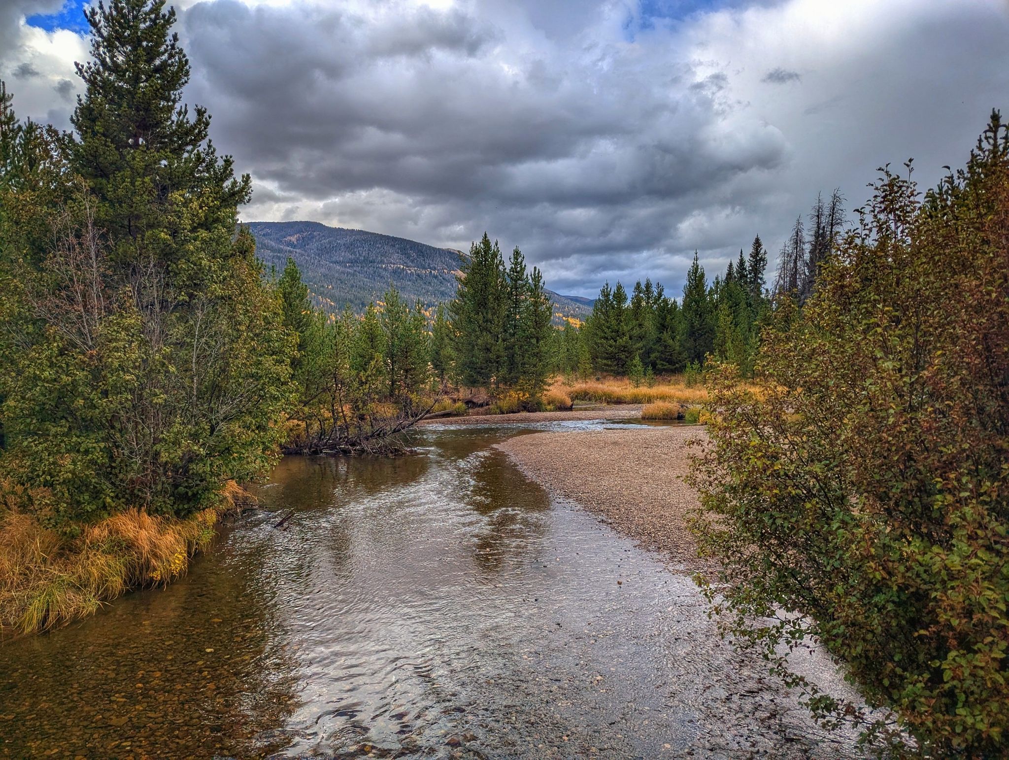 A winding river flows through a forest with mountains under a cloudy sky. - Baker Gulch to Bowen Gulch Lake