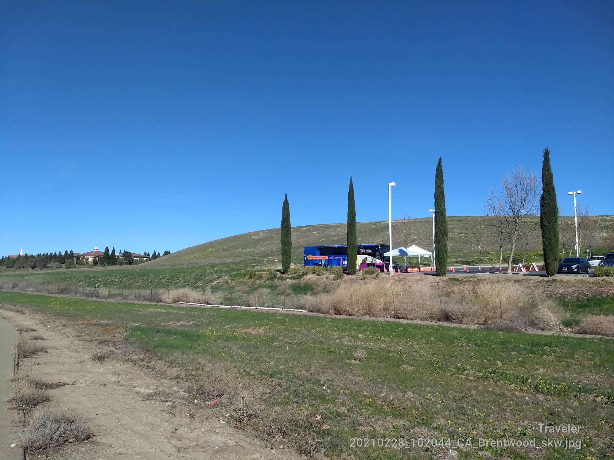 Wide grassy field leading to a hill with tall trees and a white tent. - Mokelumne Trail