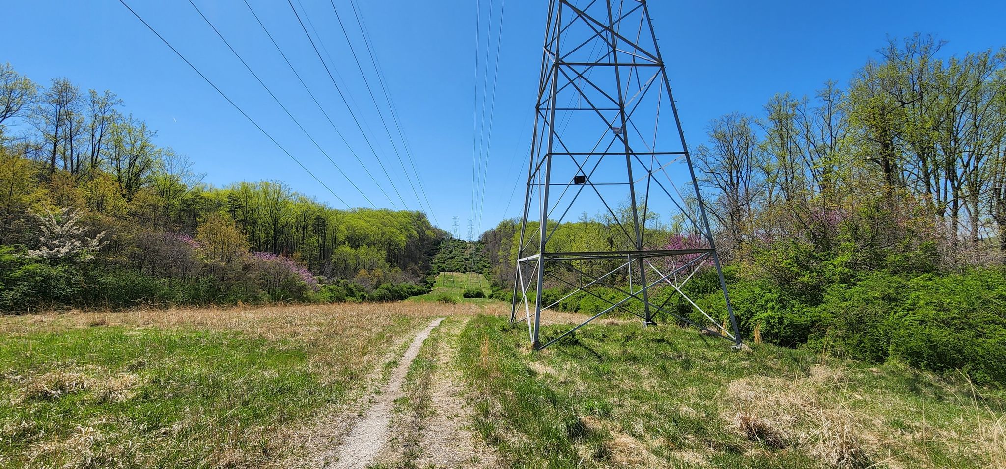 A dirt path leads past a tall power tower under a clear blue sky. - Little waterfall loop from Dulaney High School