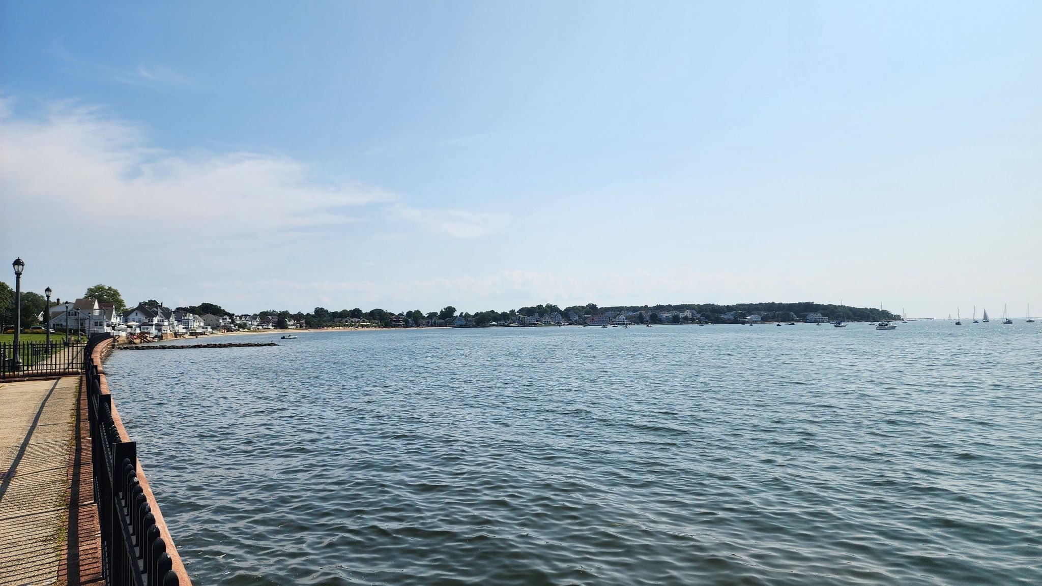 Sunny view of a calm bay with a boardwalk, distant town, and boats. - Forbes Bluff and Pardee Seawall Walk