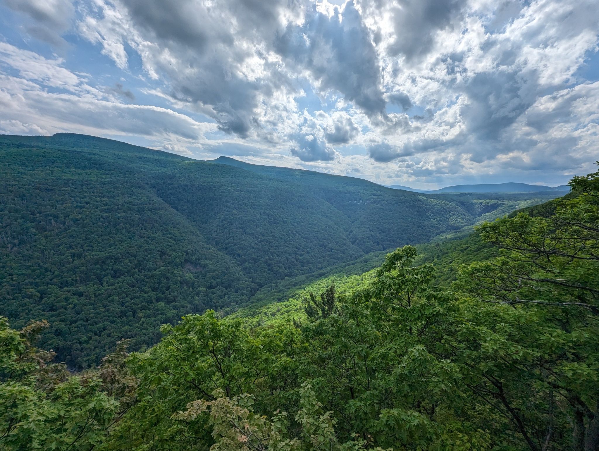Expansive view of a deep, lush green forested valley under a dramatic cloudy sky. - Inspiration Point and Kaaterskill Falls Loop