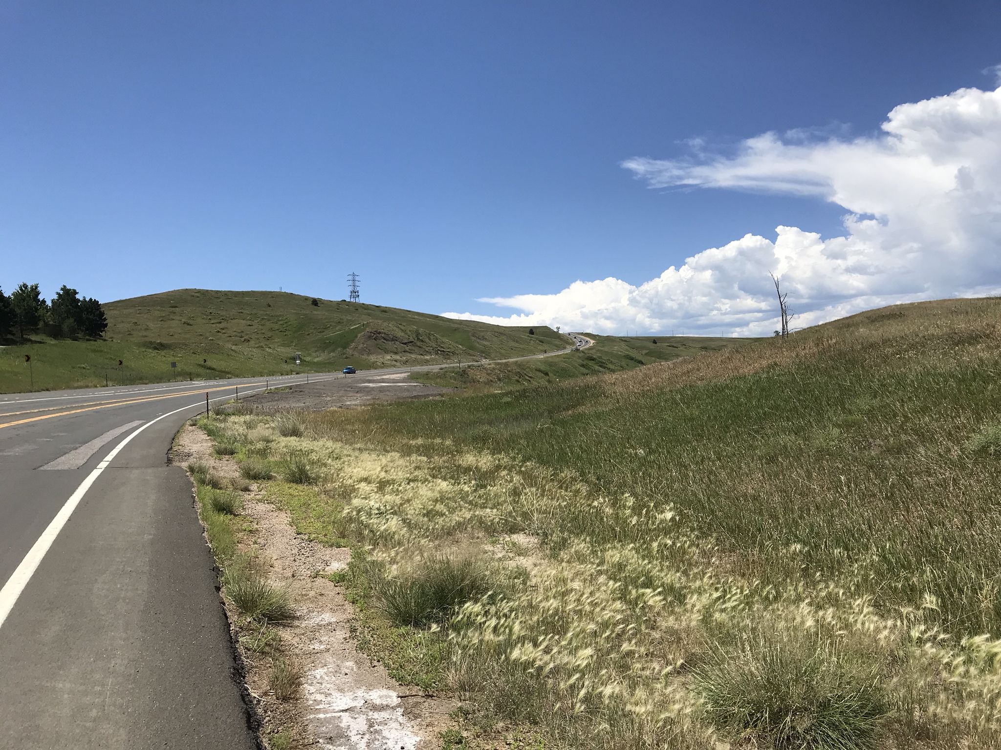 A winding road through green, grassy hills under a bright, cloudy sky. - Broomfield County High Point loop from Eldorado K-8 School