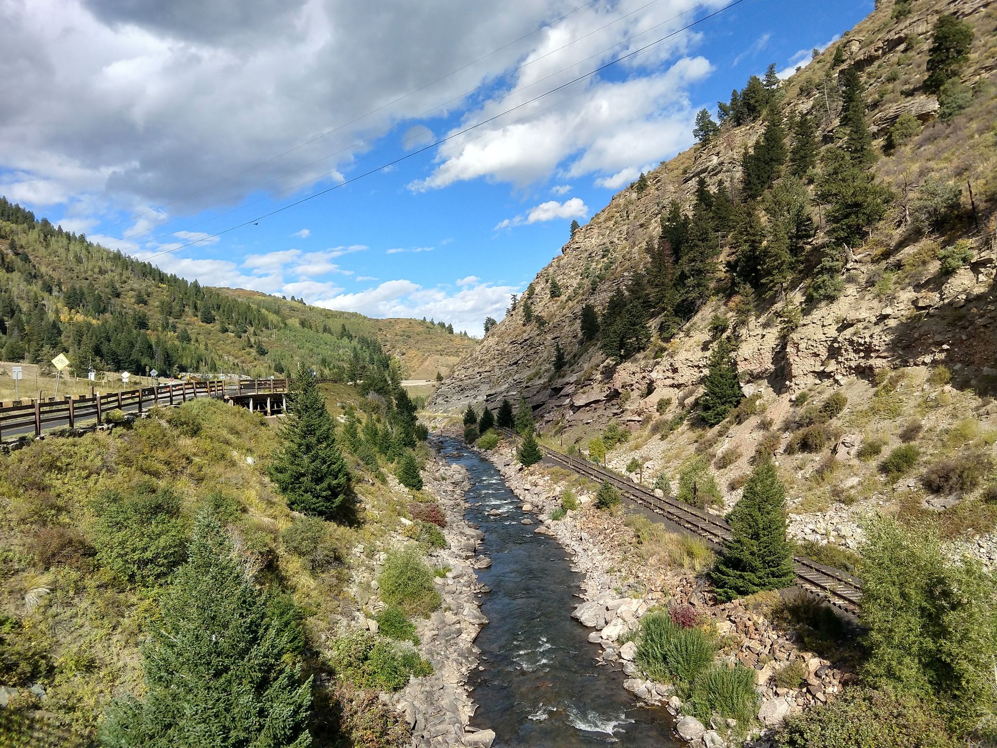 River and railroad tracks winding through a mountain valley, partly cloudy. - Gore Valley Trail