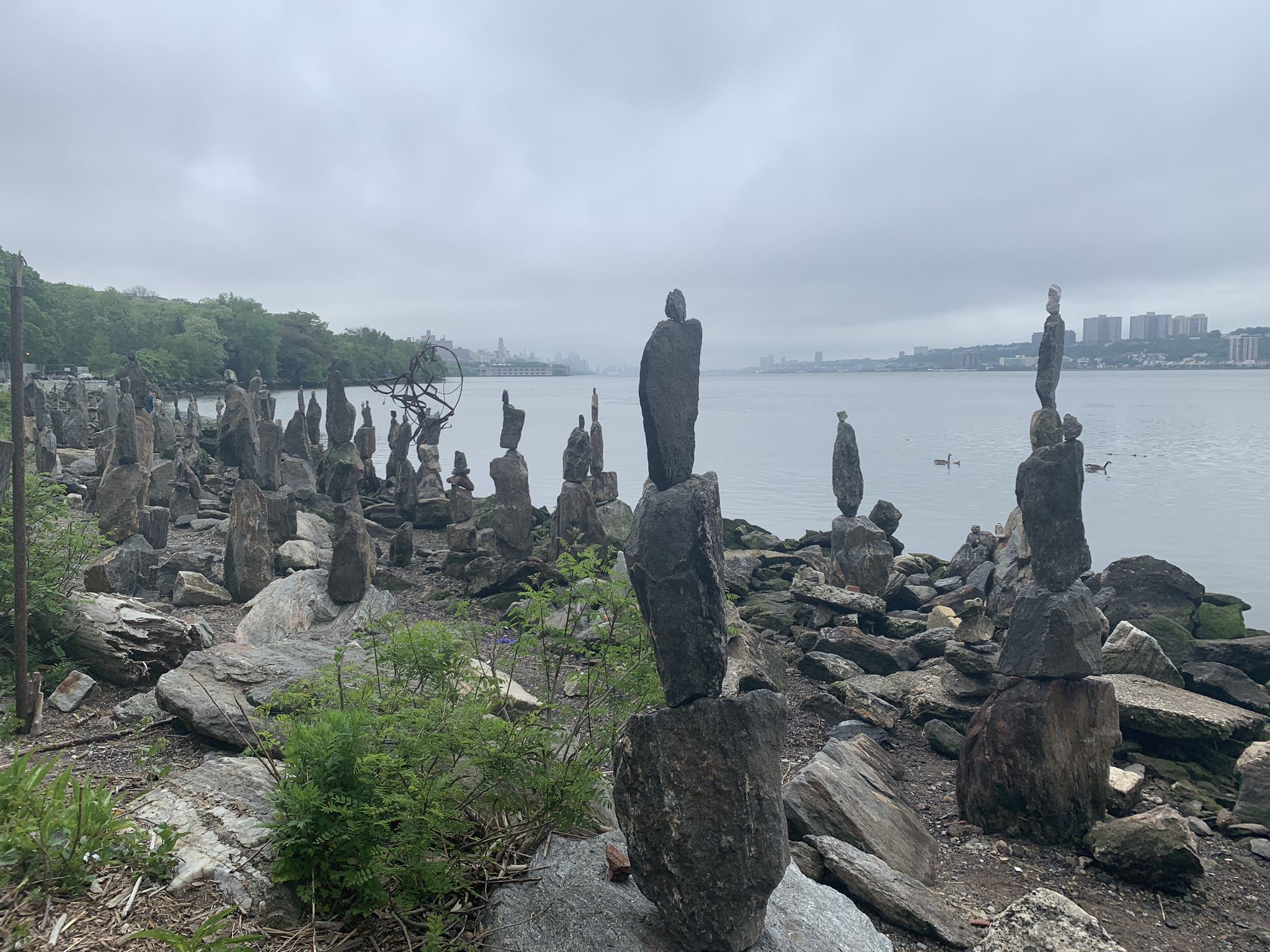 Numerous rock cairns line a rocky river shore under an overcast sky. - The Little Red Lighthouse – Fort Washington Park Greenway loop from 157th Street