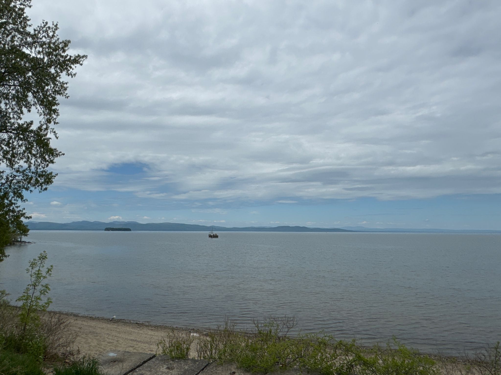 A wide body of calm water with a distant boat under a cloudy, expansive sky. - Blanchard Beach – Burlington Greenway loop from East Woods Natural Area