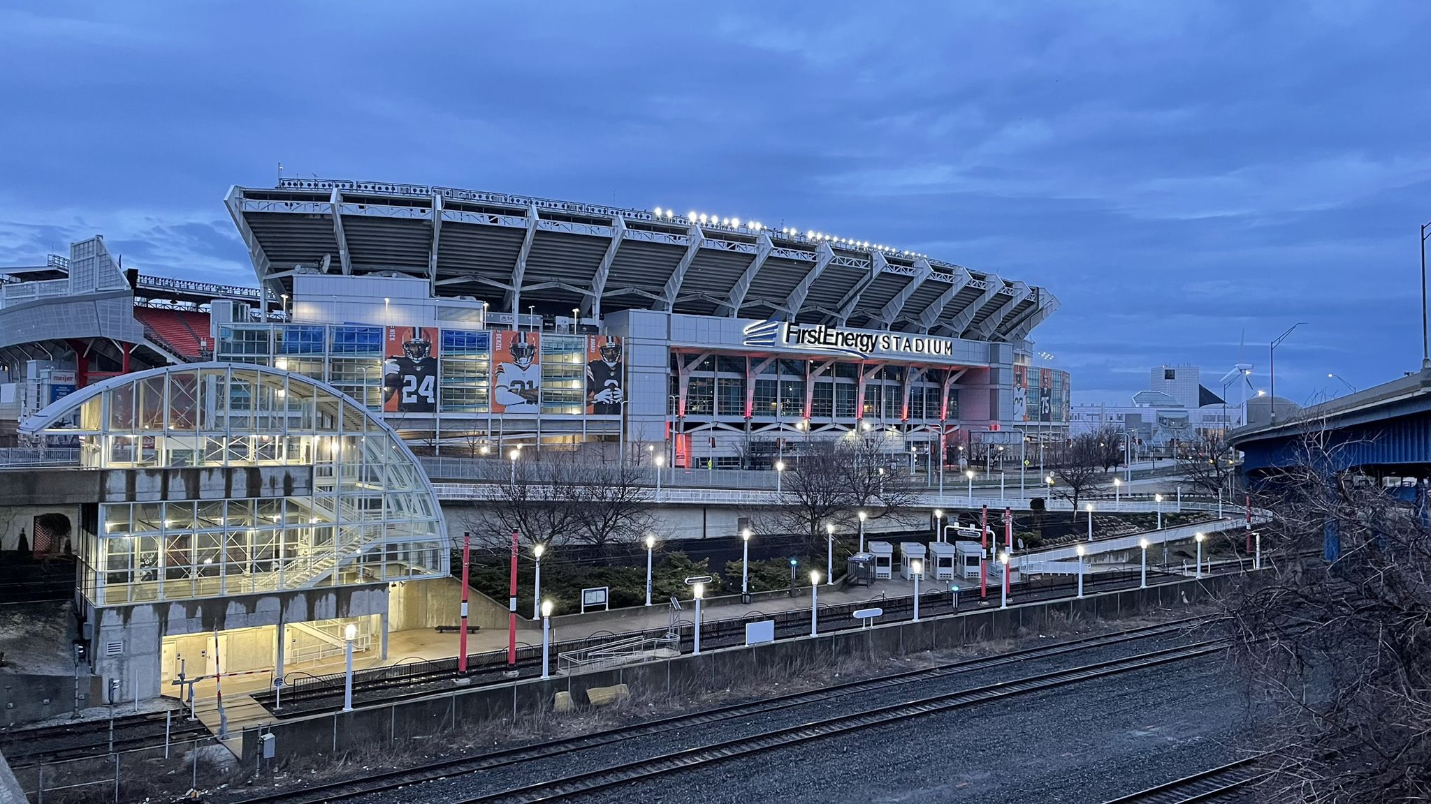 Large stadium lit up at dusk, with train tracks in the foreground. - Free Stamp Sculpture – Voinovich Bicentennial Park loop from Cleveland