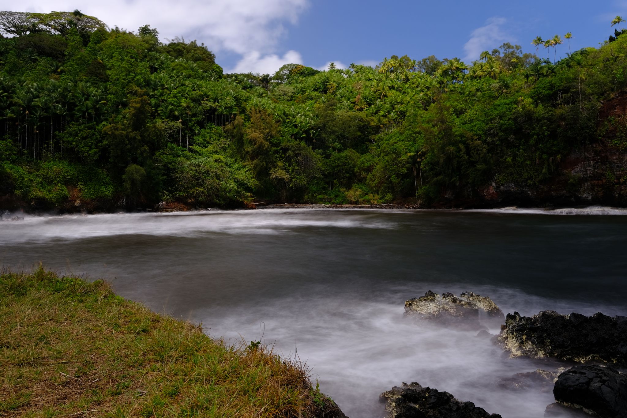 Lush green forest surrounds a calm bay with misty water under a bright sky. - Onomea Bay – Onomea Bay Viewpoint loop from Hawaii Tropical Botanical Garden