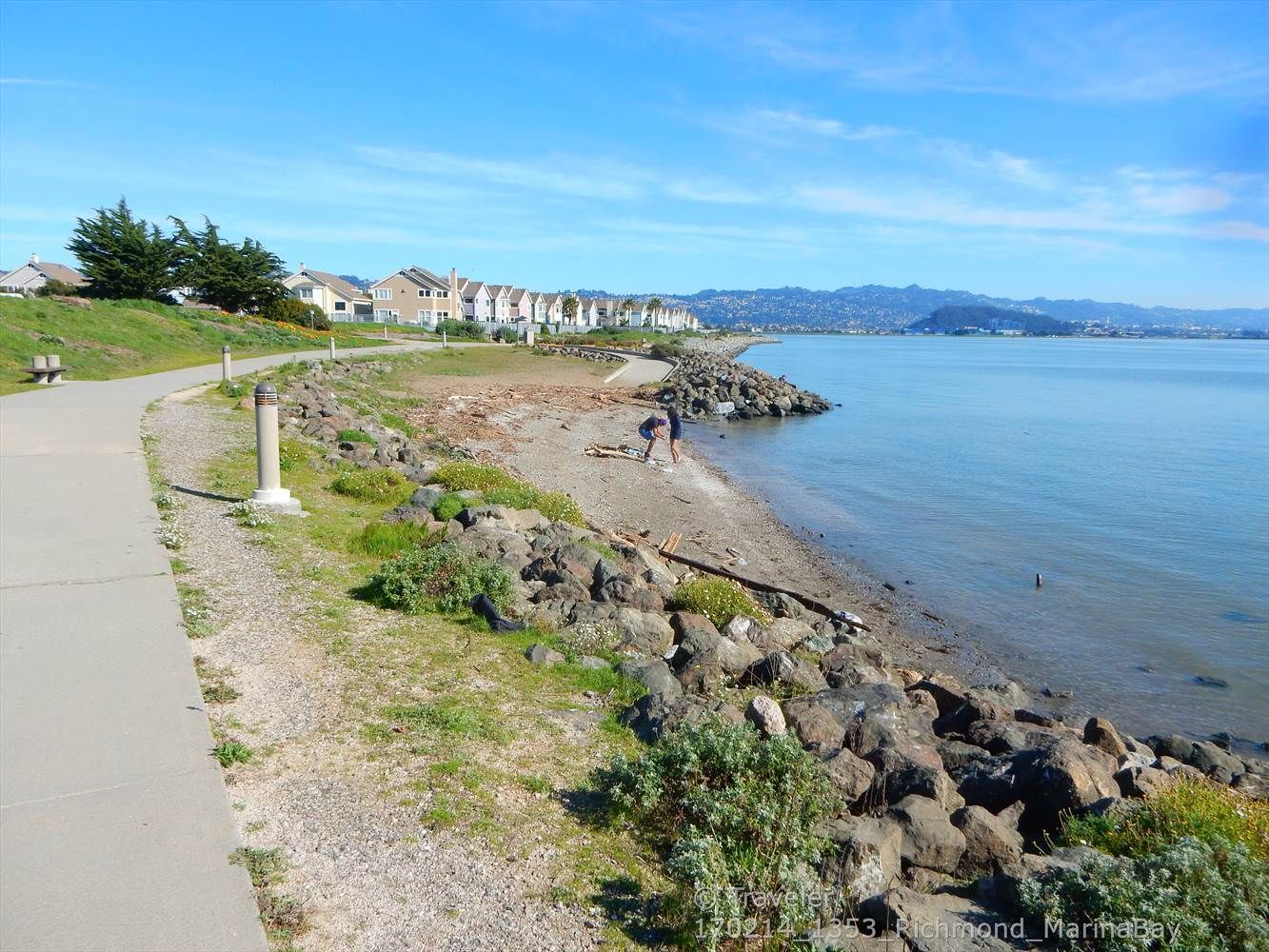 Paved path next to a rocky beach with a person walking. - Richmond Bay Trail – Shimada Friendship Park loop from Rosie the Riveter/World War II Home Front National Historical Park