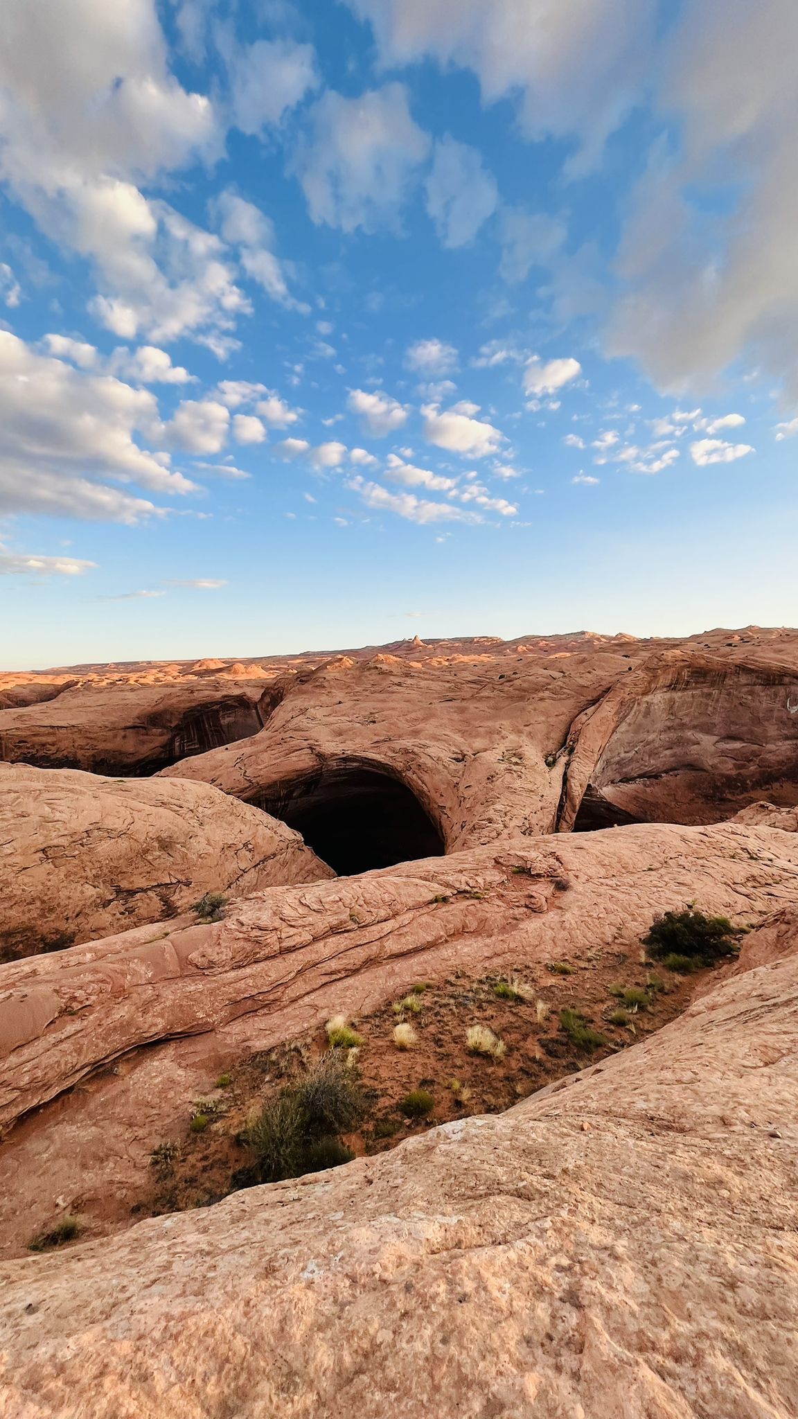 Expansive rocky desert landscape with a dark cave entrance under a cloudy sky. - Swiss Cheese Falls – Big Rock in Coyote Gulch loop from Crack-in-the-Wall
