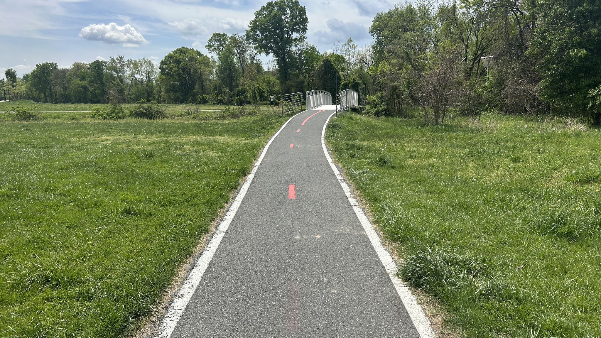 Paved path through green grassy fields leading to a distant bridge. - Sligo Creek Trail – Melrose Park Pump Track loop from Wheaton