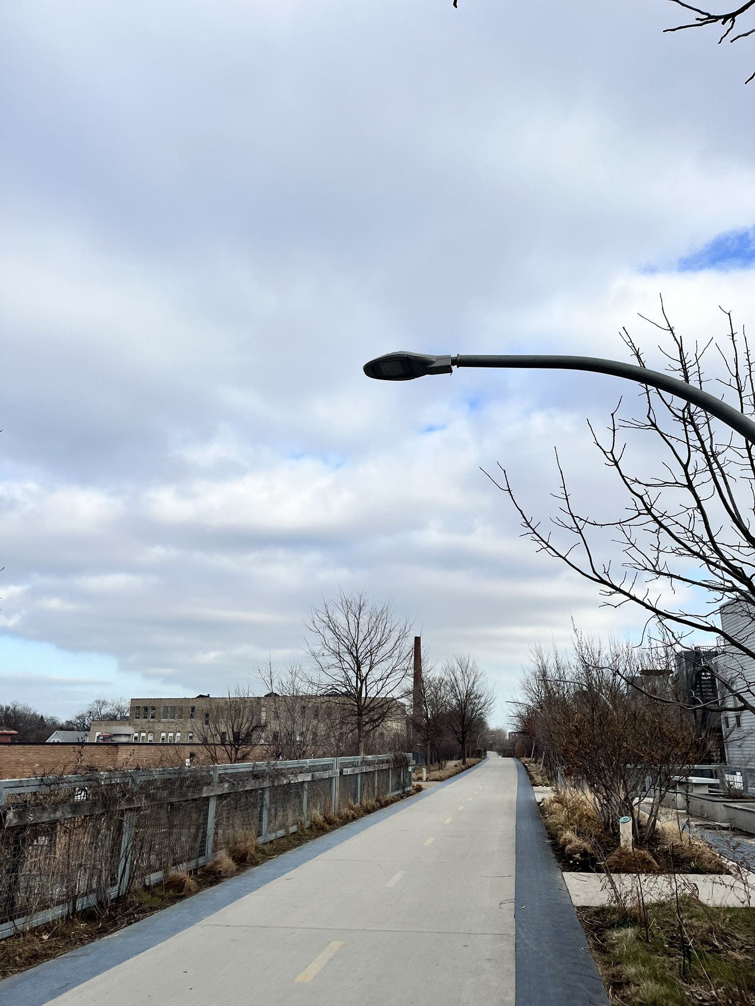 A paved path with bare trees and distant buildings under a cloudy sky. - Bloomingdale Trail