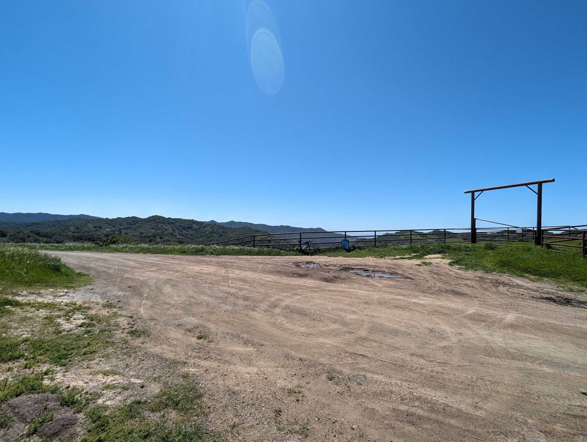 A wide dirt road leads to a fence with distant green hills under a clear sky. - Santa Rita Road