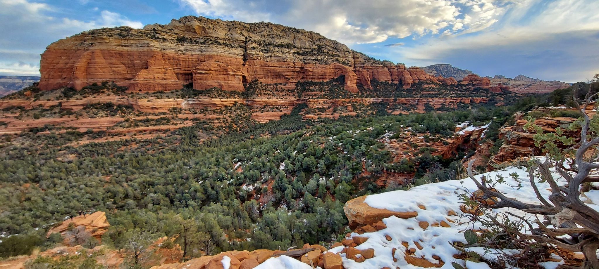 Panoramic view of red rock formations, green trees, and snowy patches under cloudy sky. - Devil's Bridge Trail via Dry Creek Road