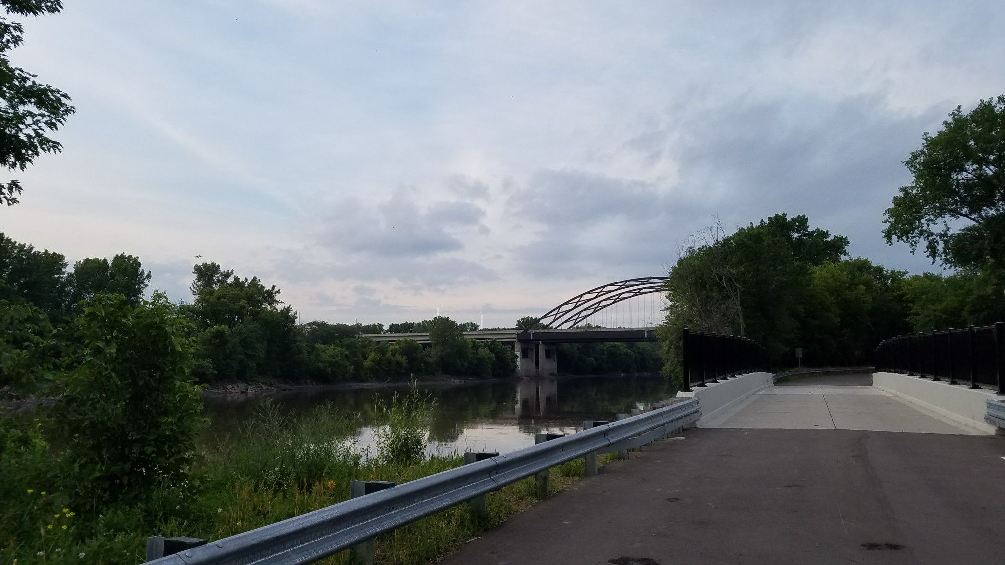 Arch bridge over a river, seen from a paved path on a cloudy day. - Minnesota River Greenway