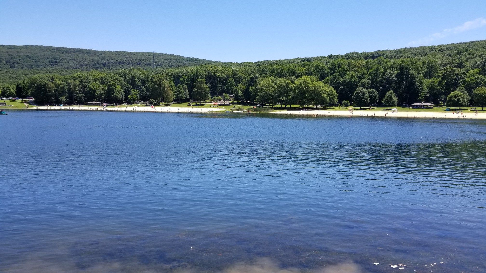 Wide blue lake with a distant sandy beach and green forested hills. - Greenbrier Lake loop