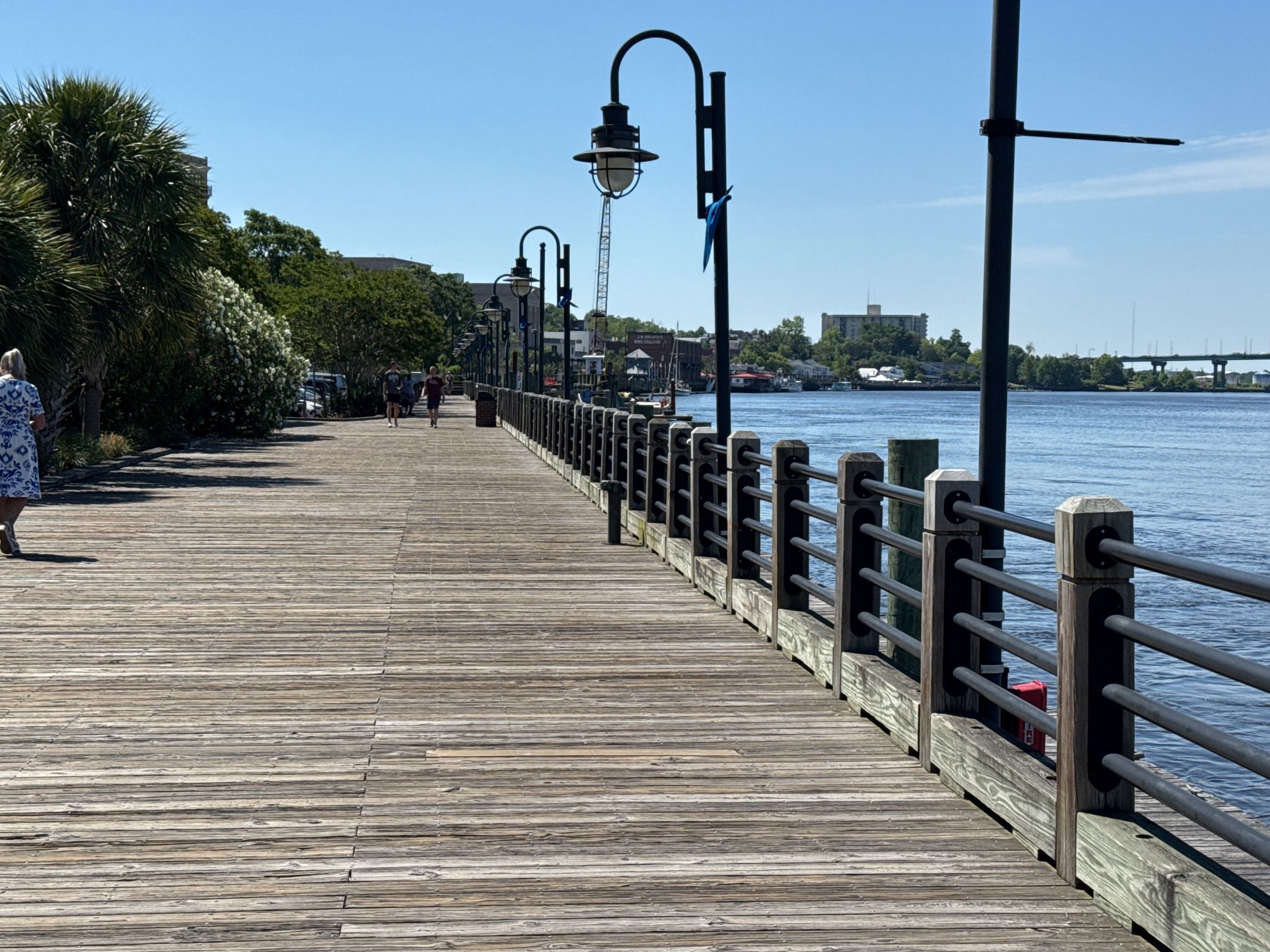 Long wooden boardwalk along a river with people walking under a sunny sky. - Railroad Museum – View of USS North Carolina loop from Wilmington